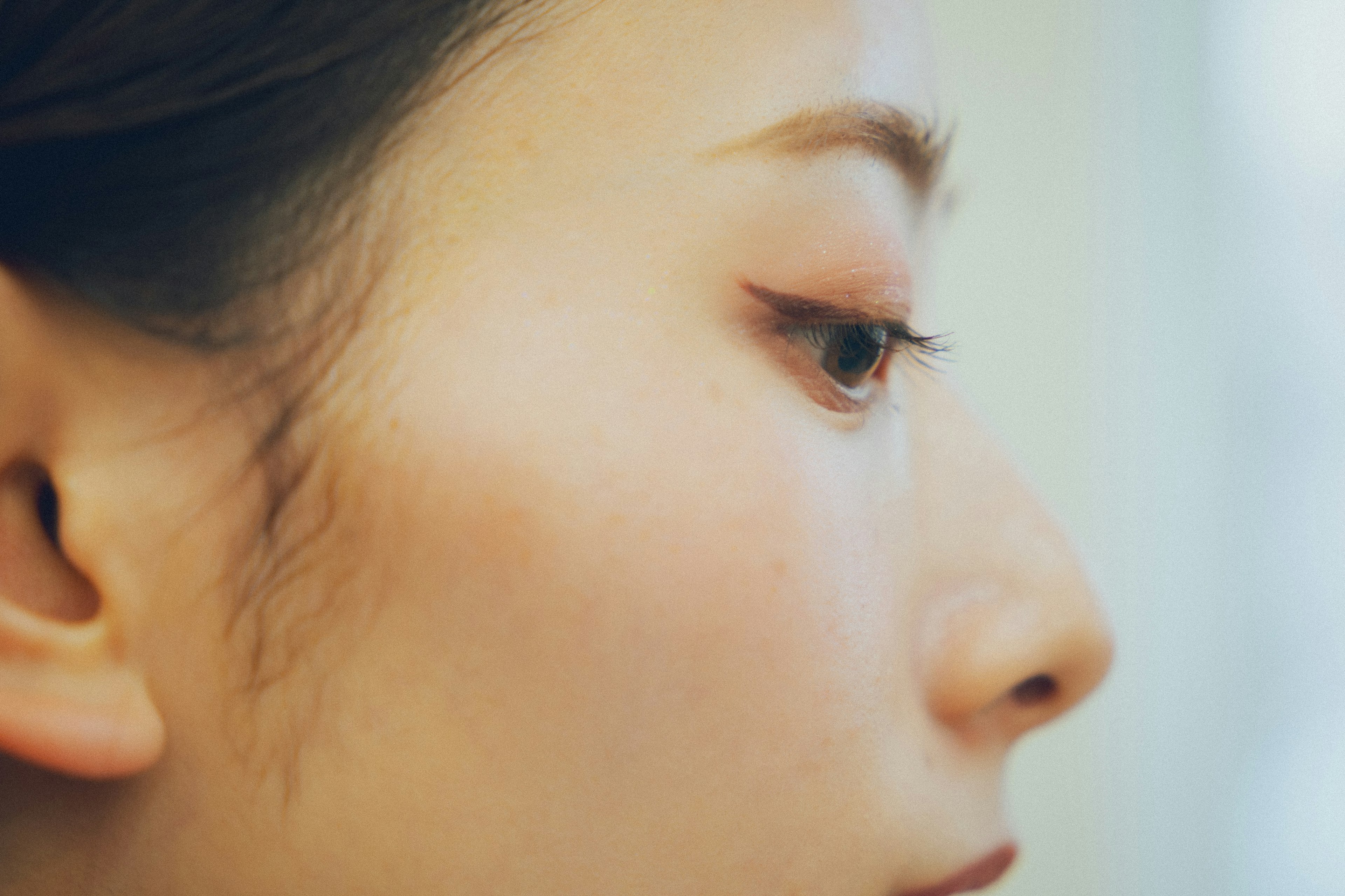 Close-up of a woman's profile showcasing soft skin and beautiful eyelashes with a subtle background