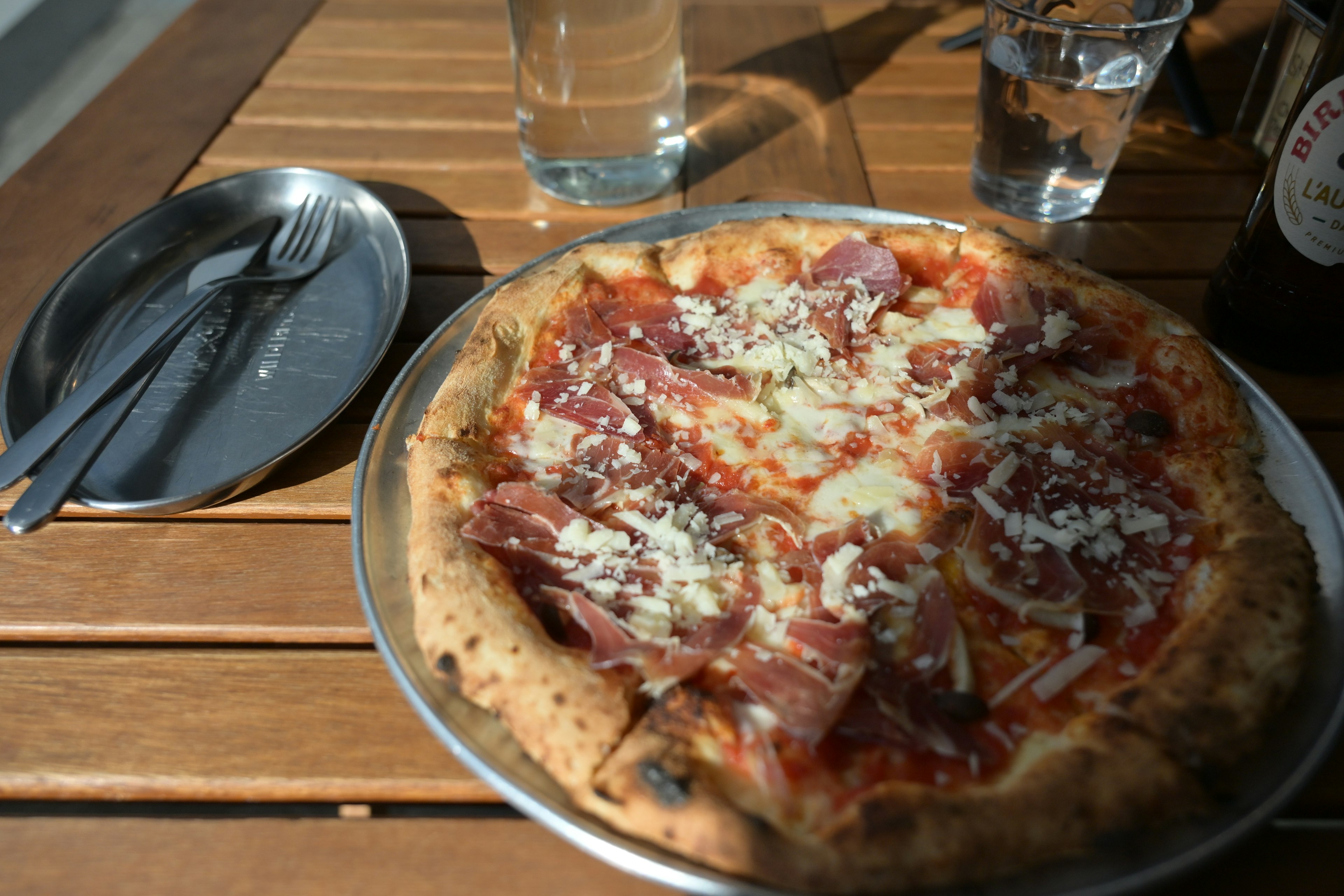 A pizza topped with cheese and salami on a wooden table with drinks