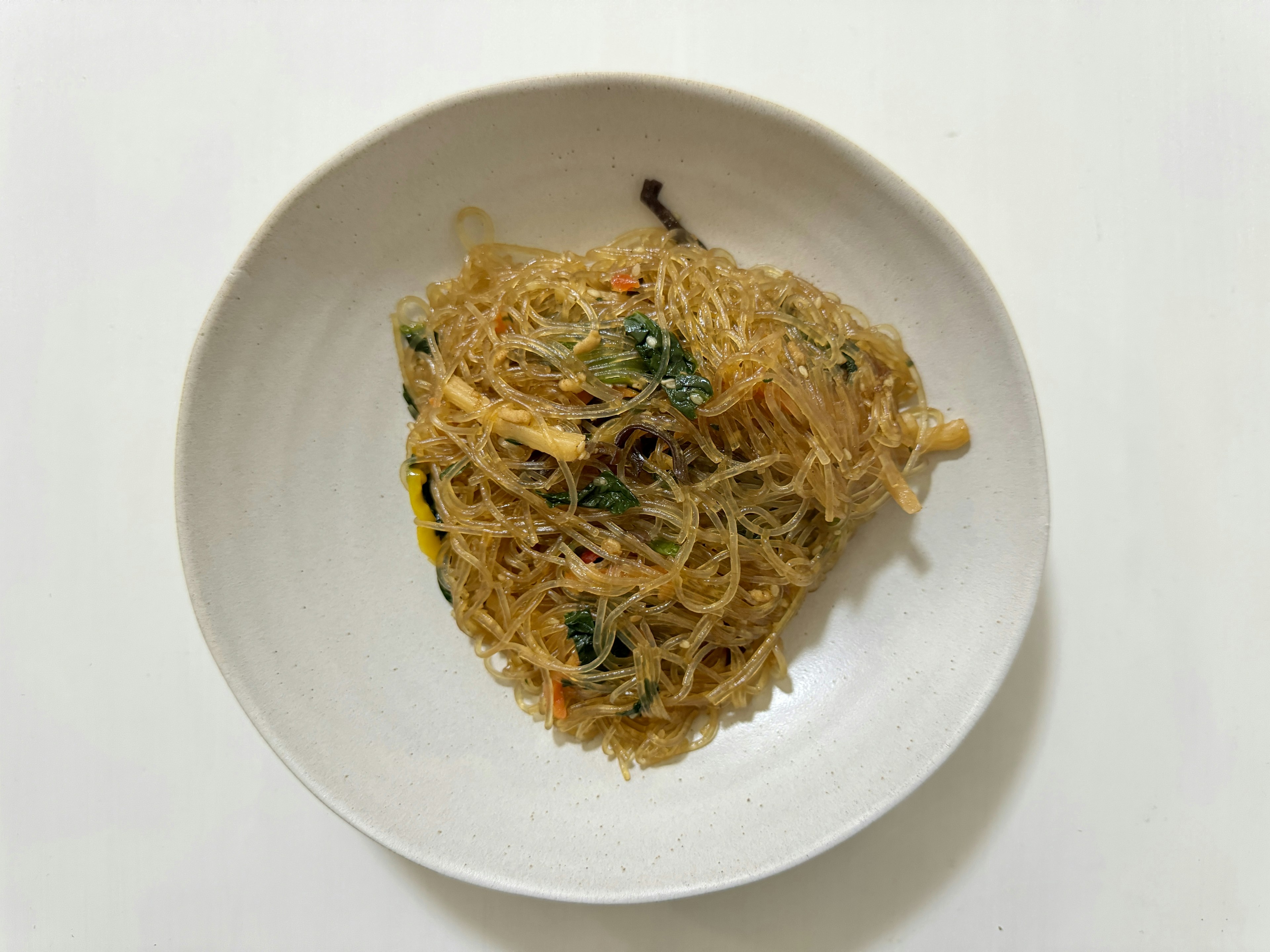 Un piatto di noodles di vetro saltati con verdure su un piatto bianco