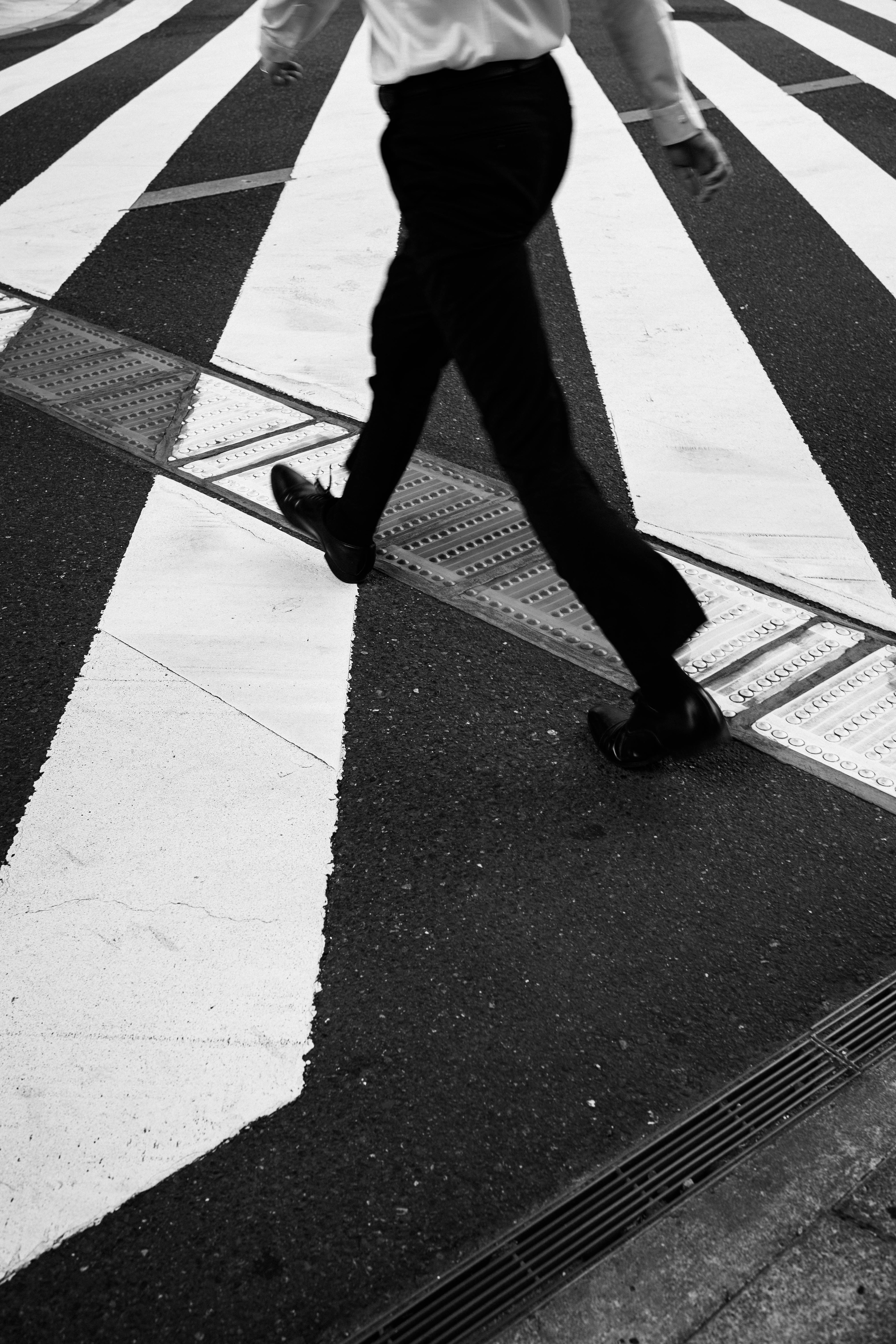 Los pies de un hombre caminando sobre un paso de cebra en blanco y negro