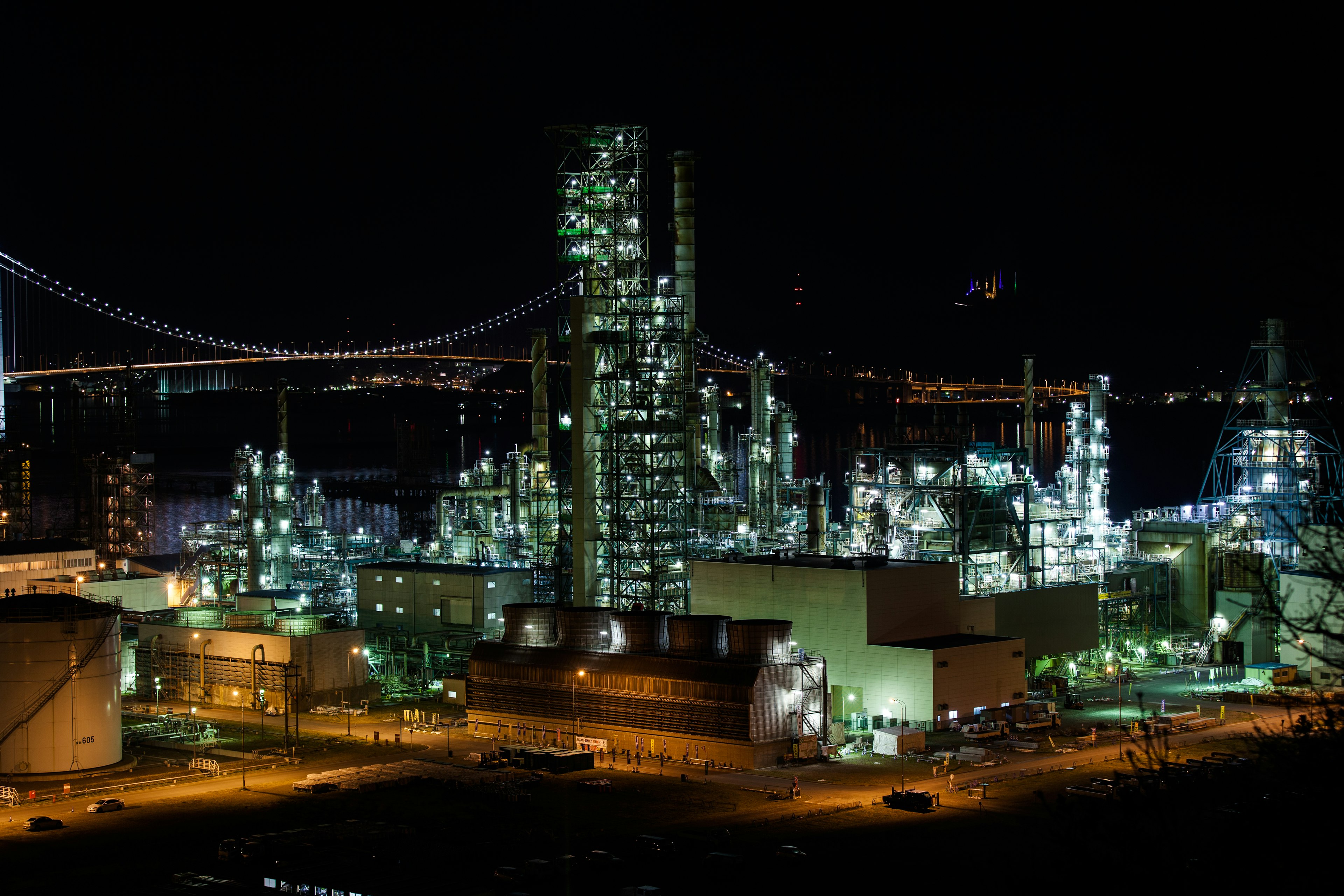 Night view of an industrial complex illuminated with lights and Rainbow Bridge in the background