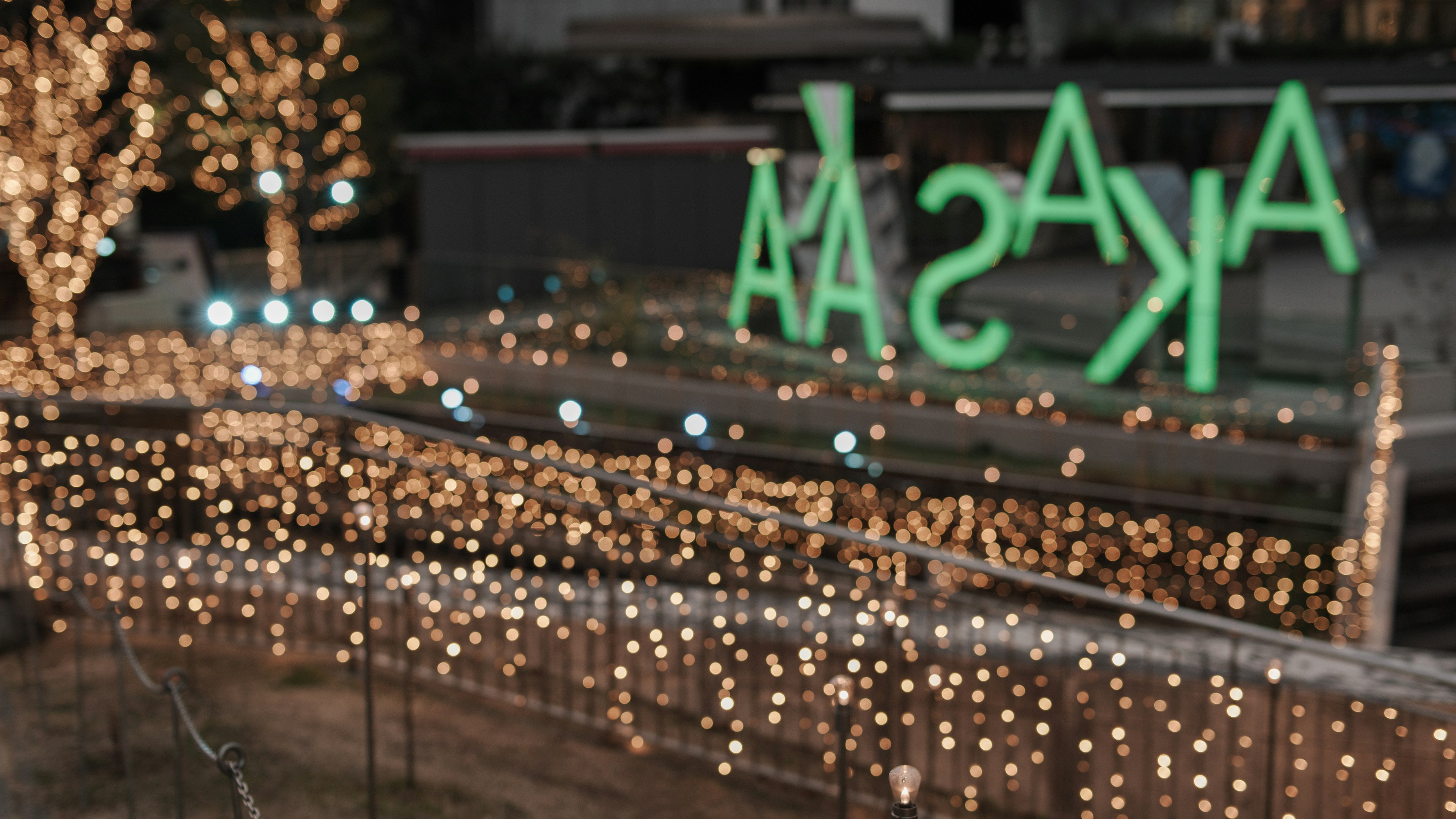 Scène nocturne avec un panneau vert portant le mot AKASA et des lumières décoratives