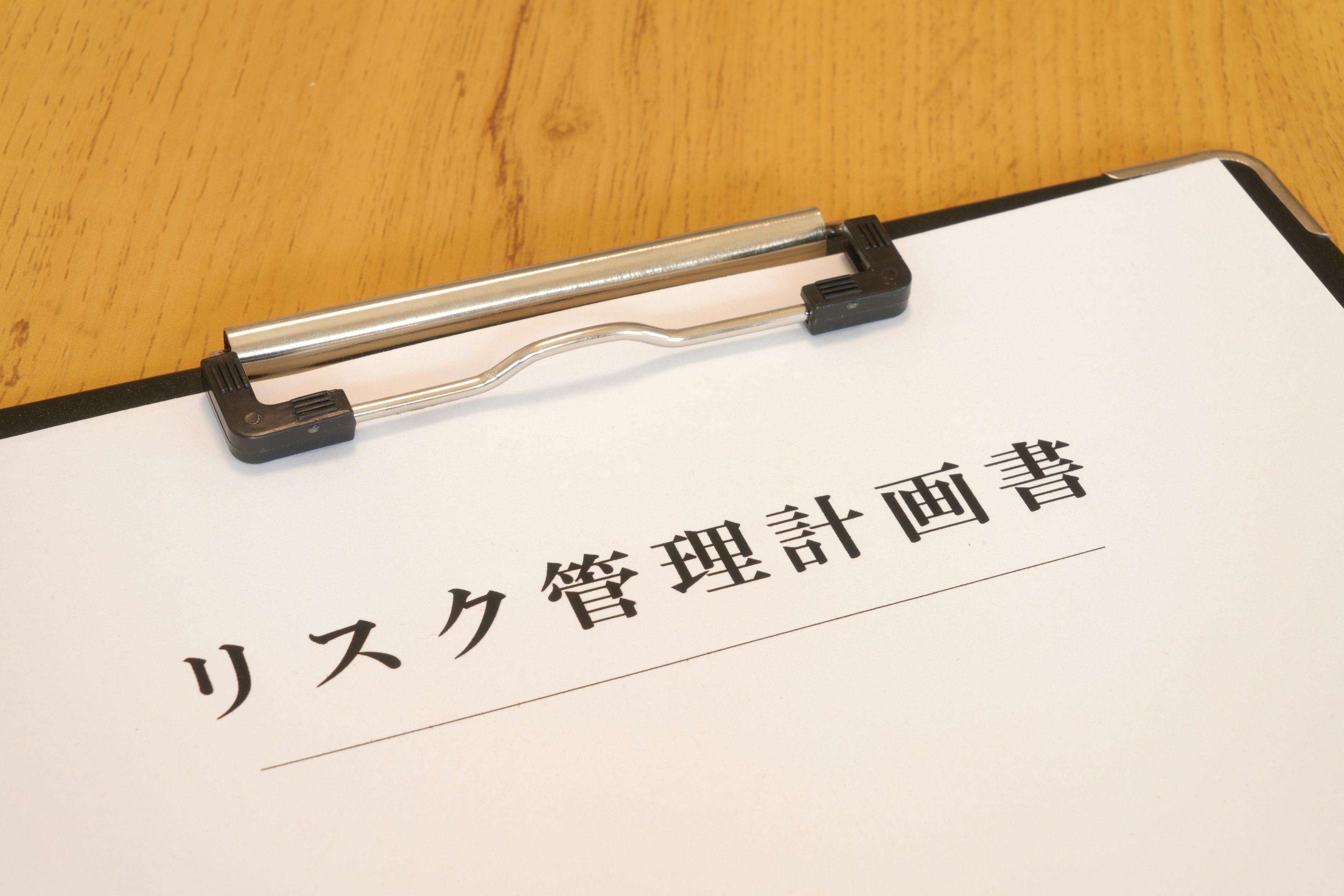 A clipboard with a document titled Risk Management Plan resting on a wooden table