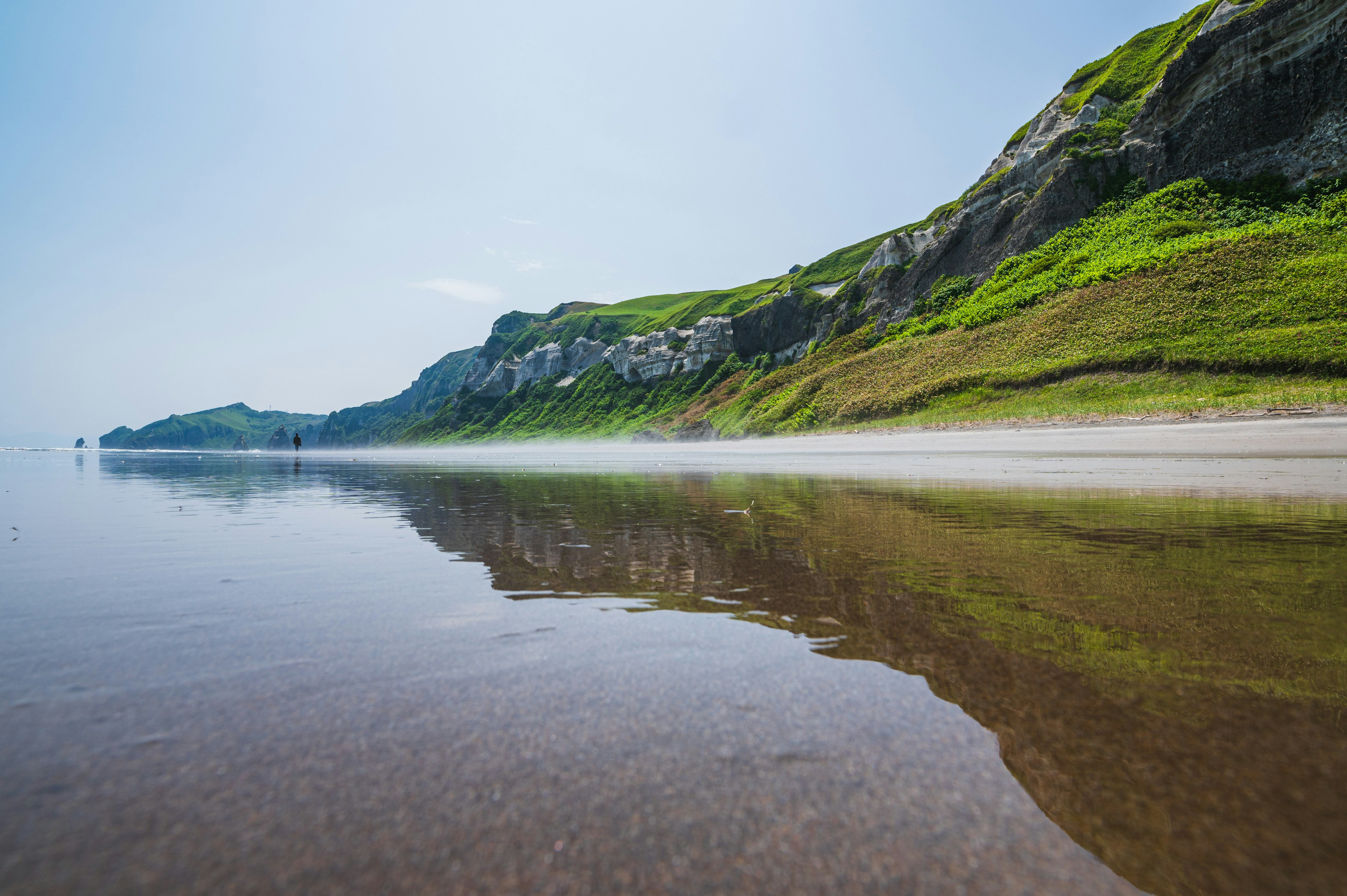 Tranquil beach scene with a beautiful coastline and lush green hills reflecting in calm water