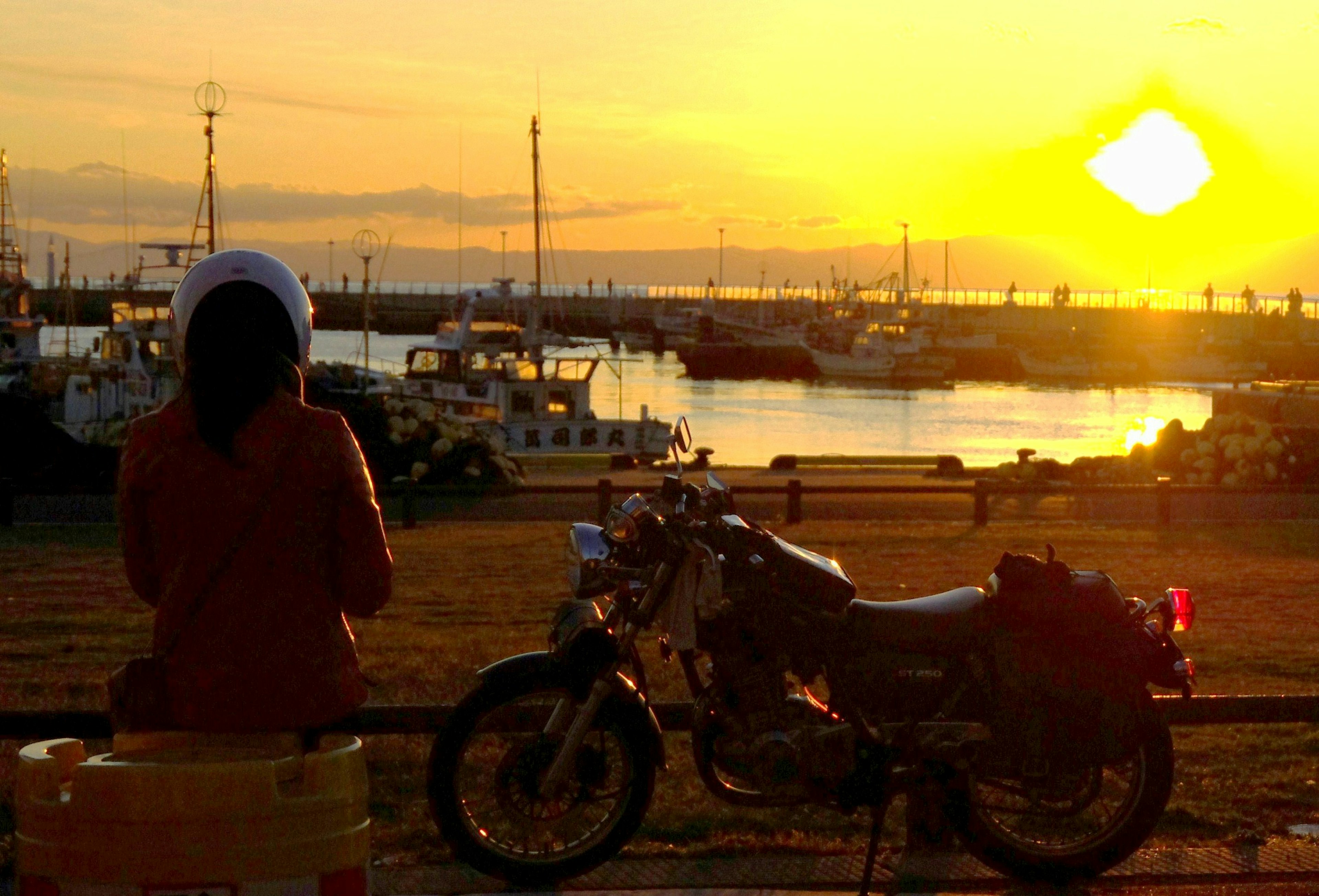 Mujer sentada junto a una motocicleta mirando el atardecer