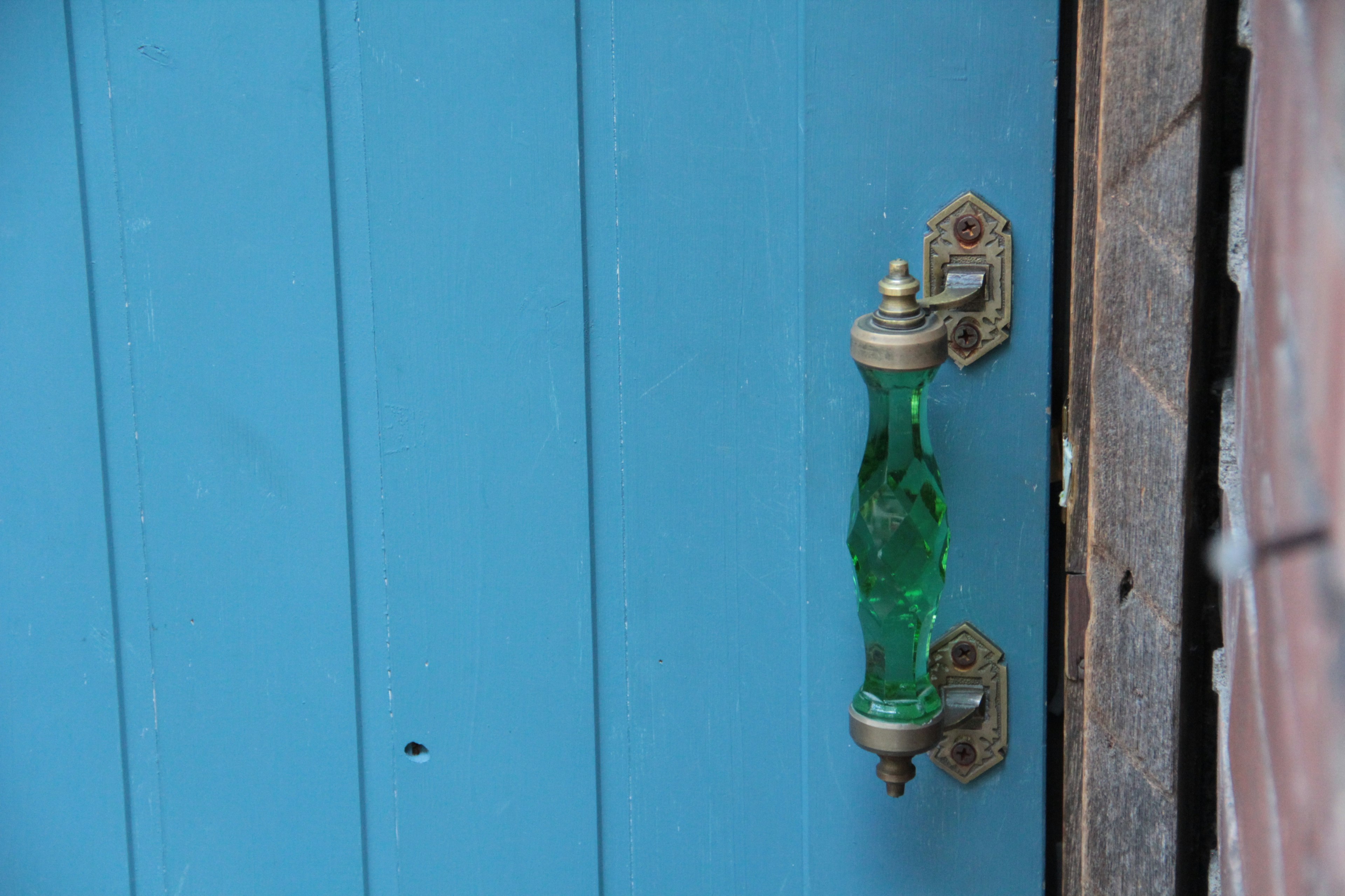 Green glass door handle on a blue door with metal fixtures