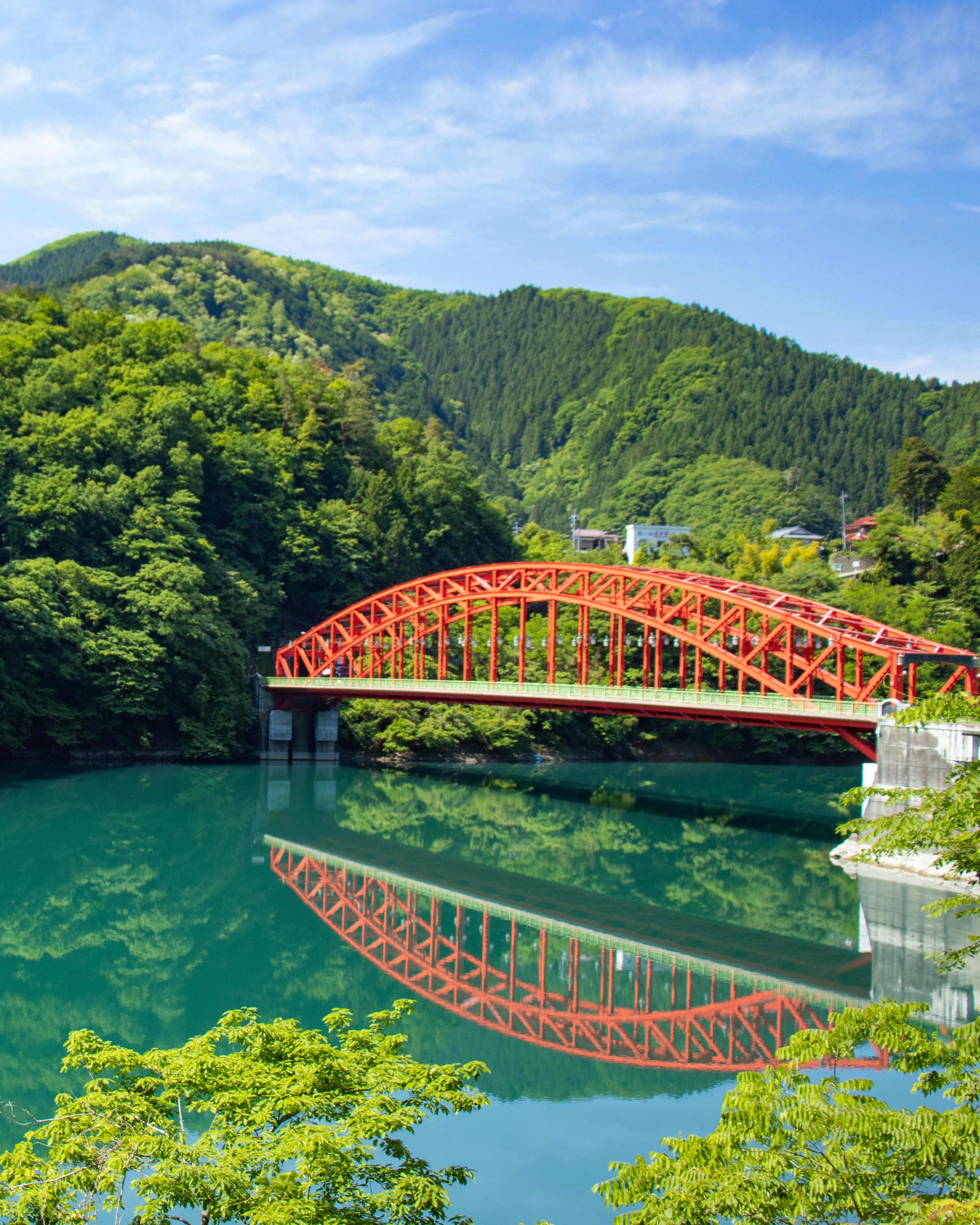 Red arch bridge surrounded by lush green mountains and its reflection