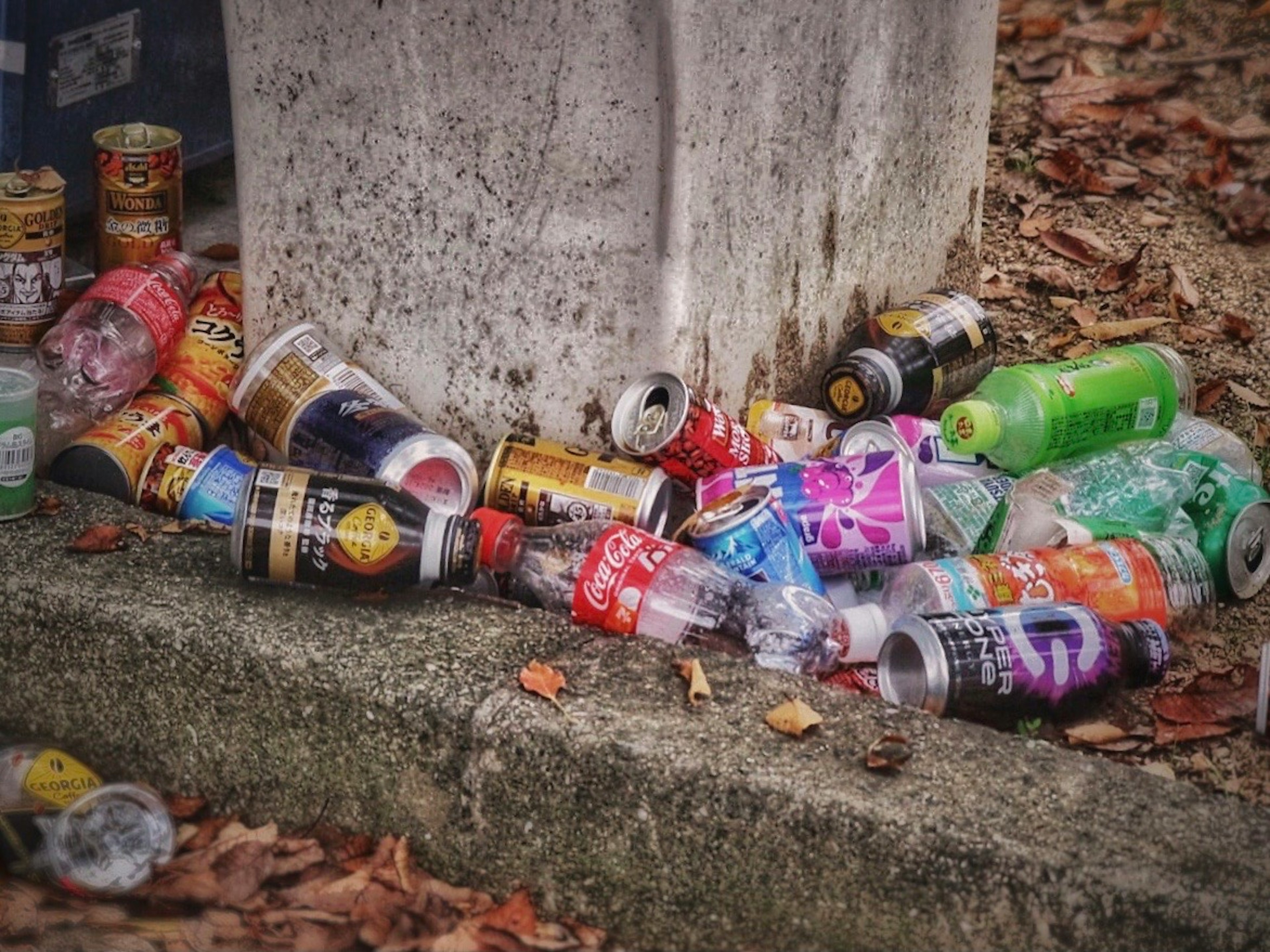 Scattered beverage containers on the ground near a concrete post