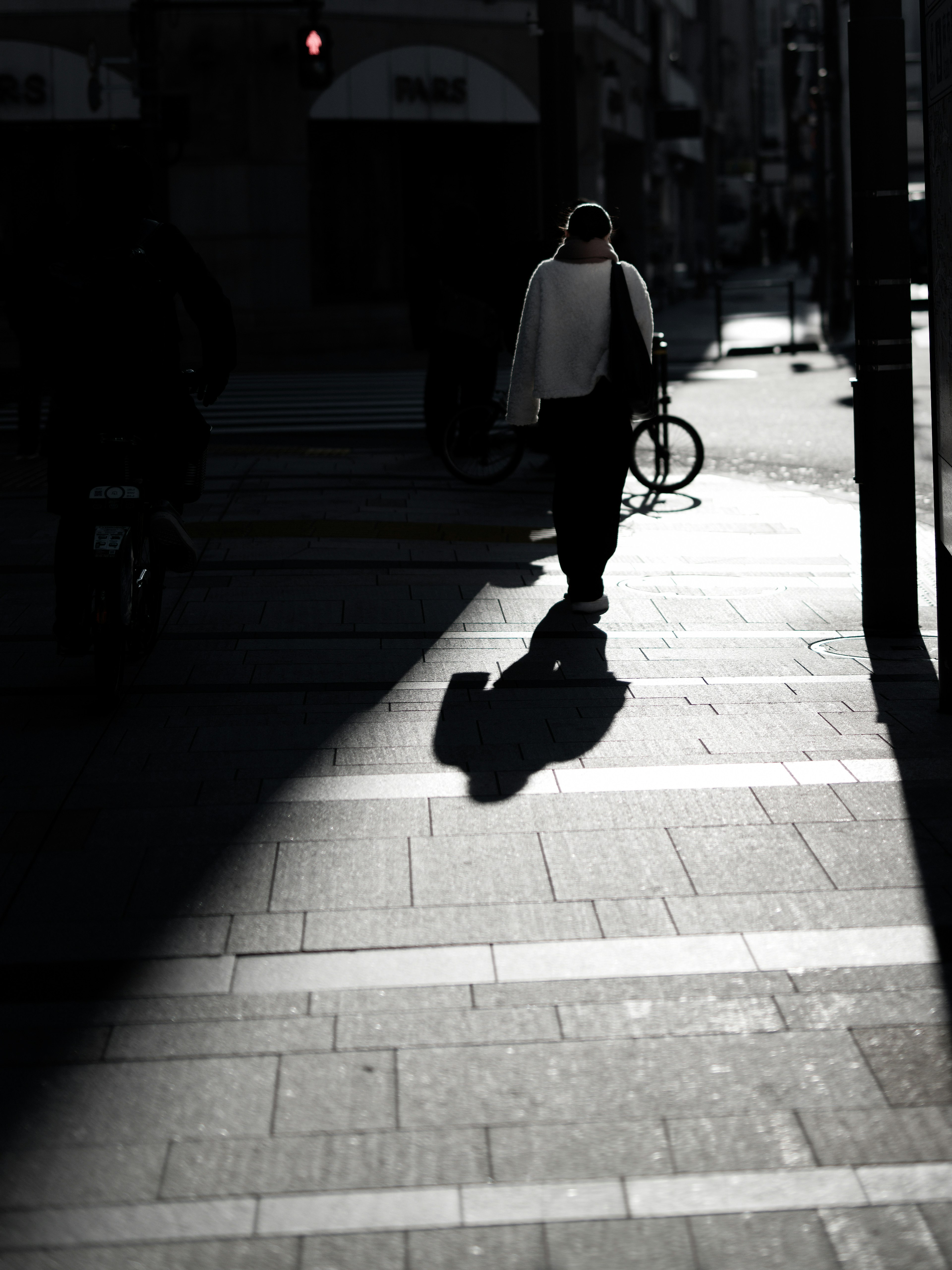 A person walking in shadows with a bicycle visible in an urban setting