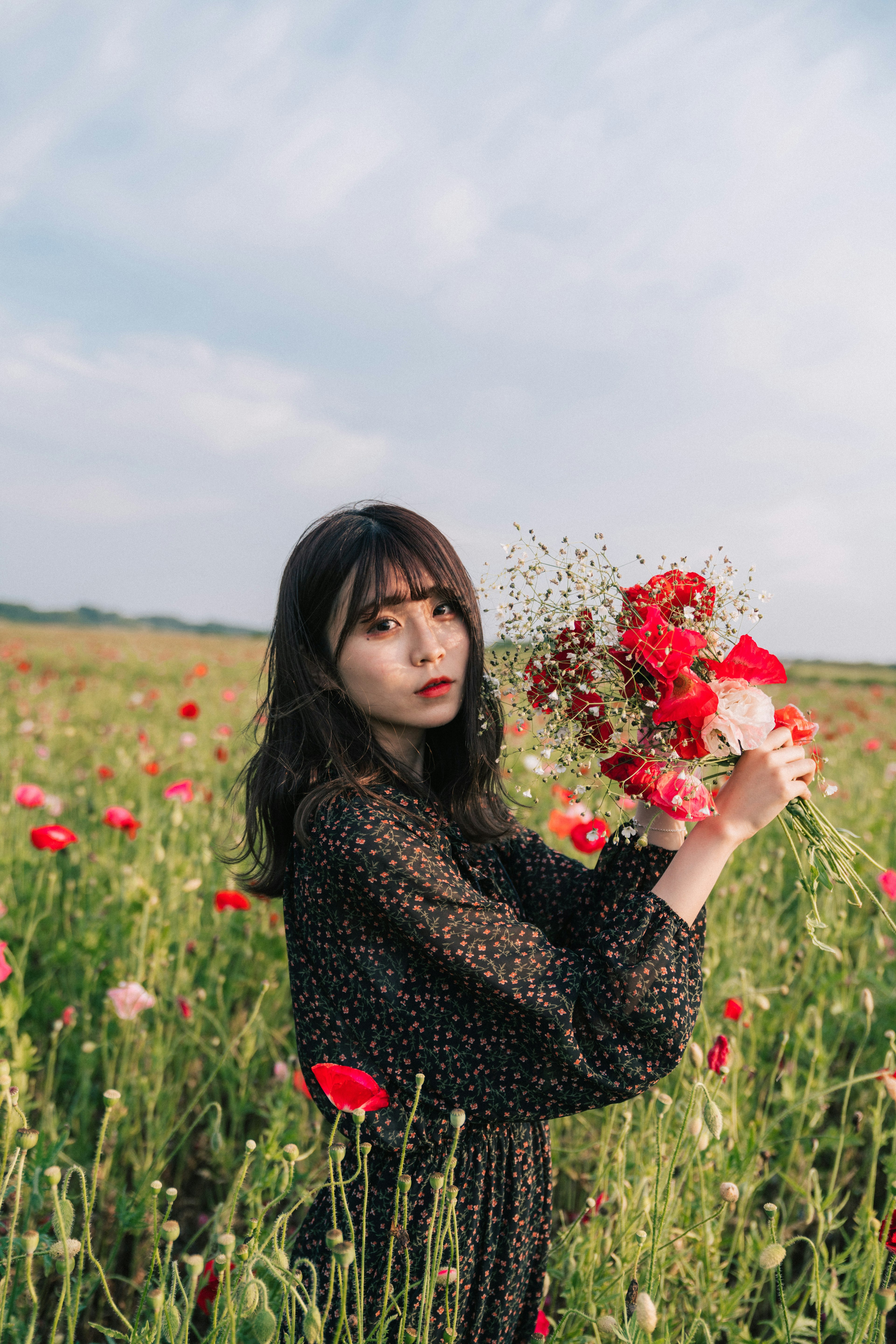 Frau mit einem Blumenstrauß steht in einem Mohnfeld