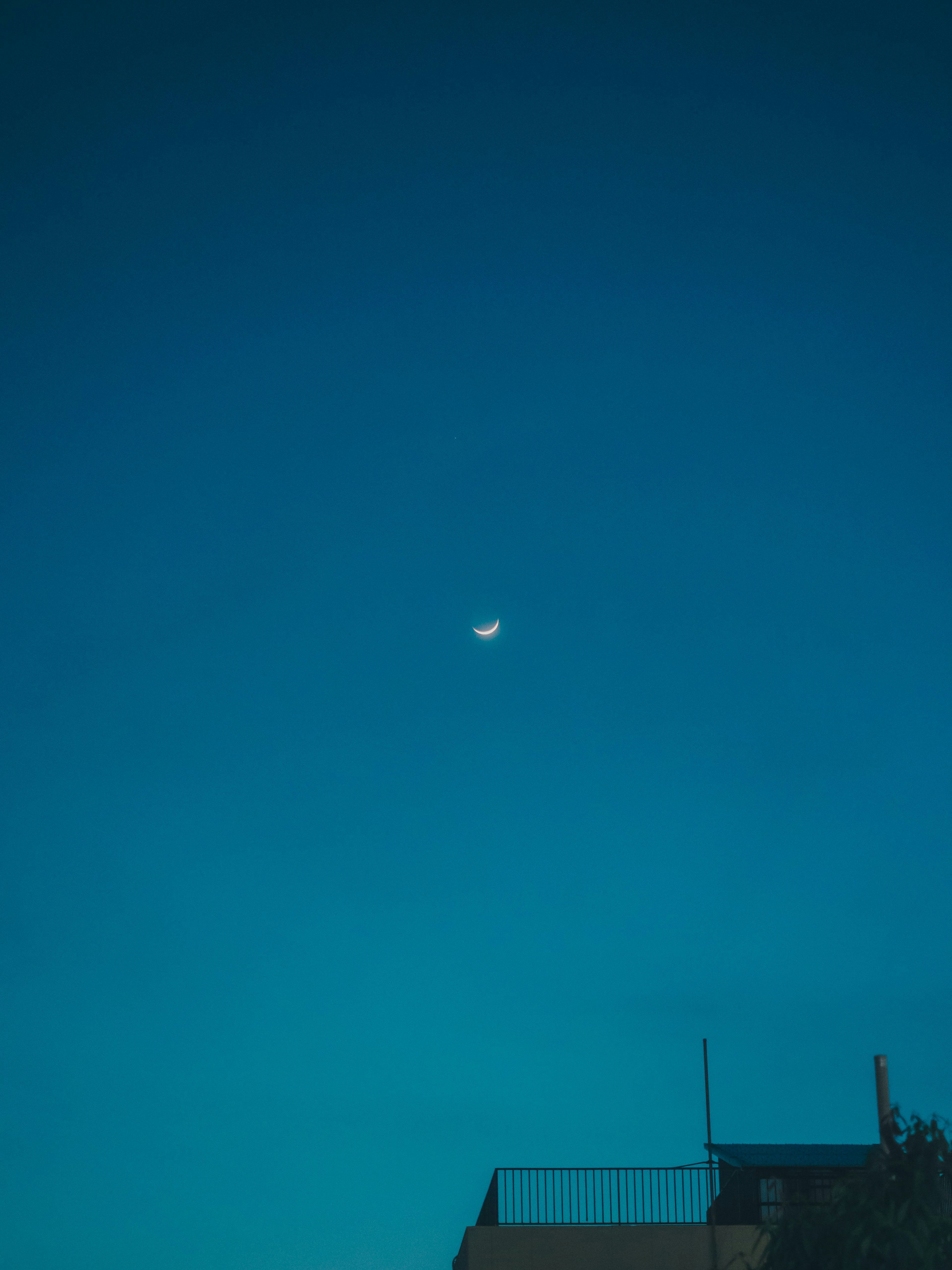 Thin crescent moon in a blue sky above a building silhouette
