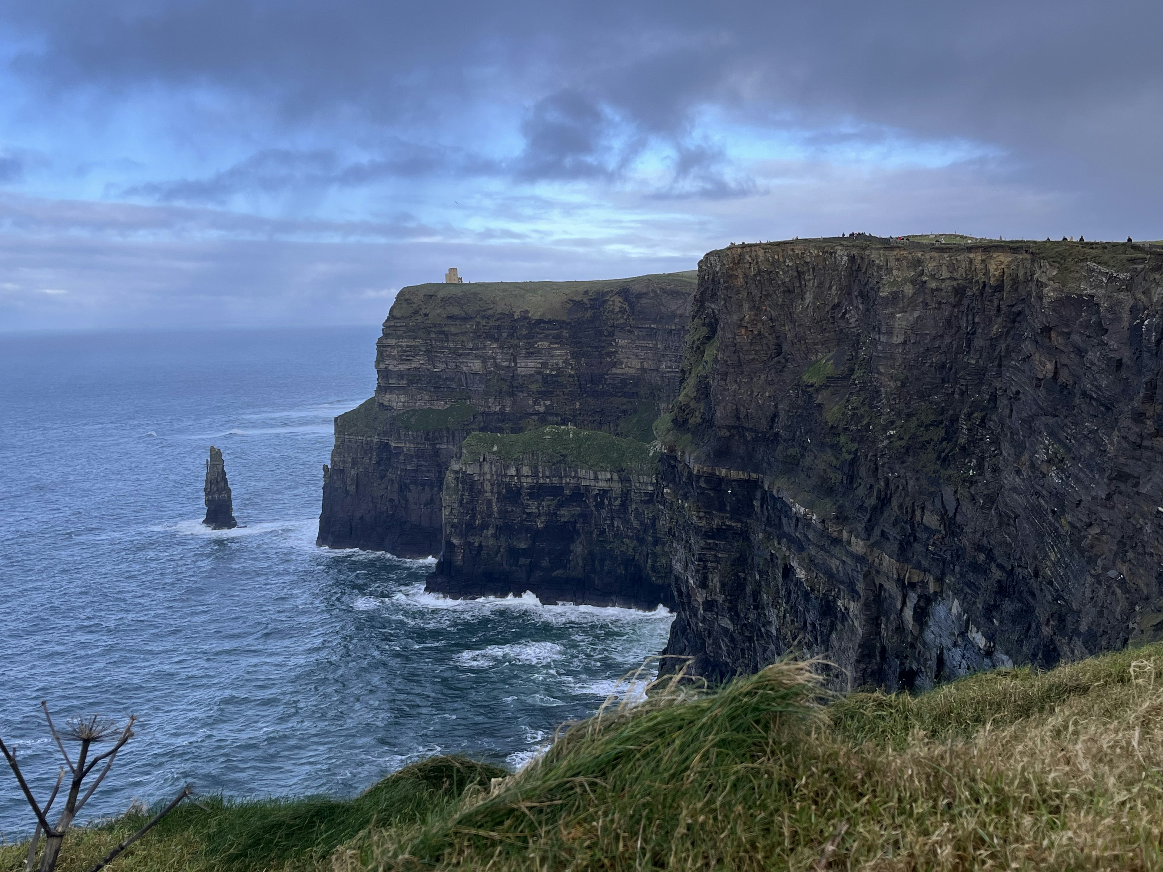 Cliffside view over the ocean featuring a distant rock formation