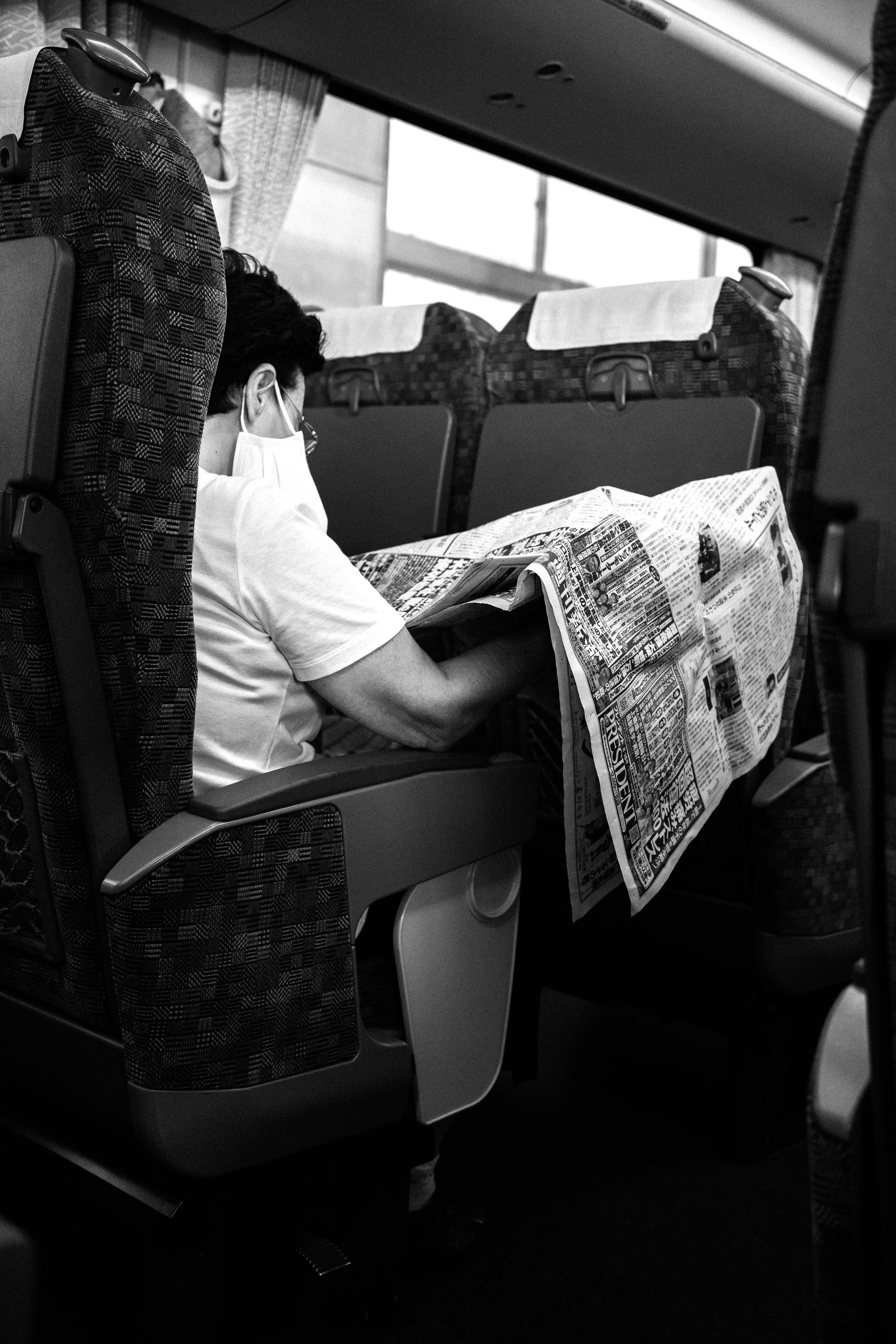 A person reading a newspaper on a bus seat