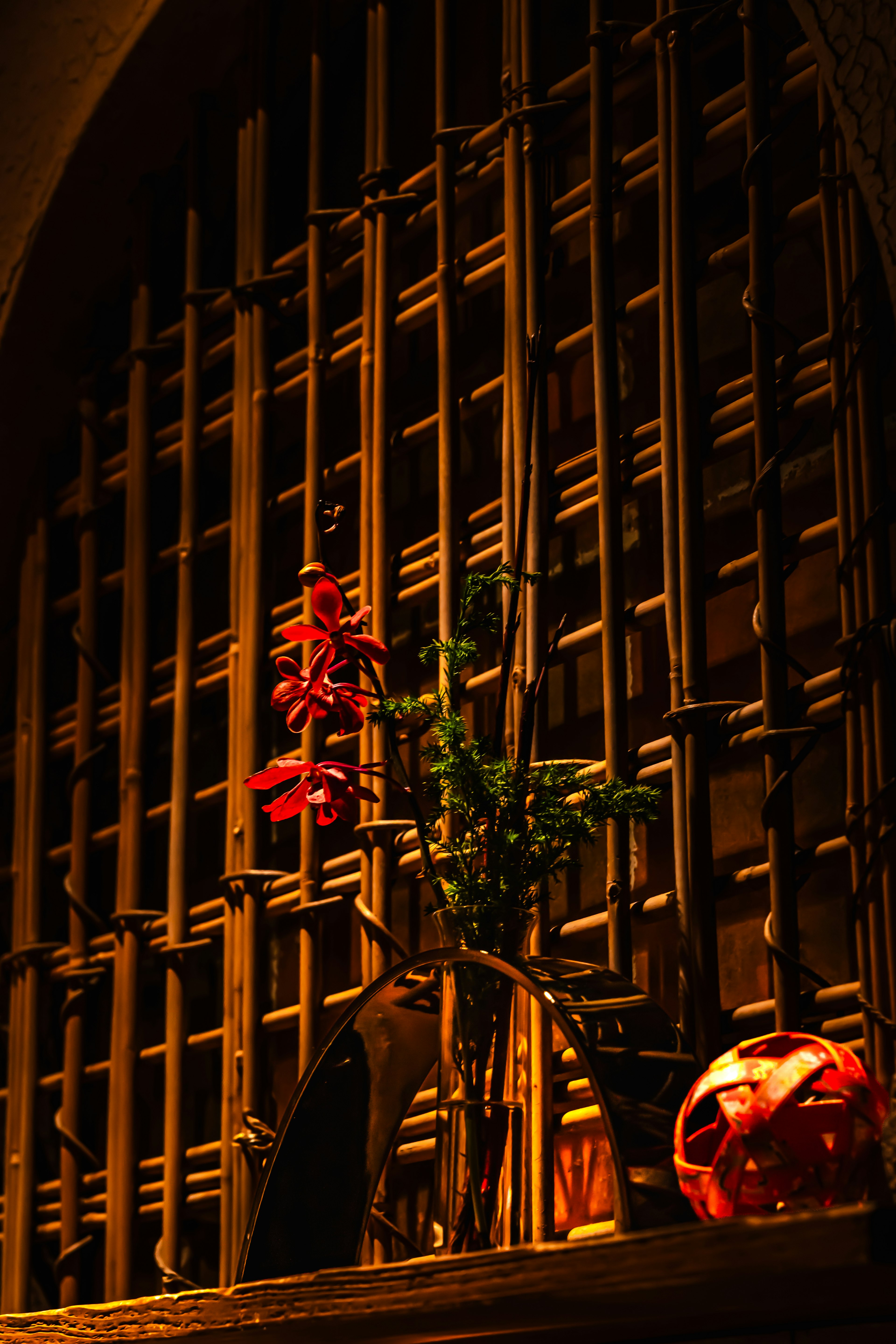 Ein ruhiges Interieur mit roten Blumen und grünen Blättern vor einem Holzlattengitter