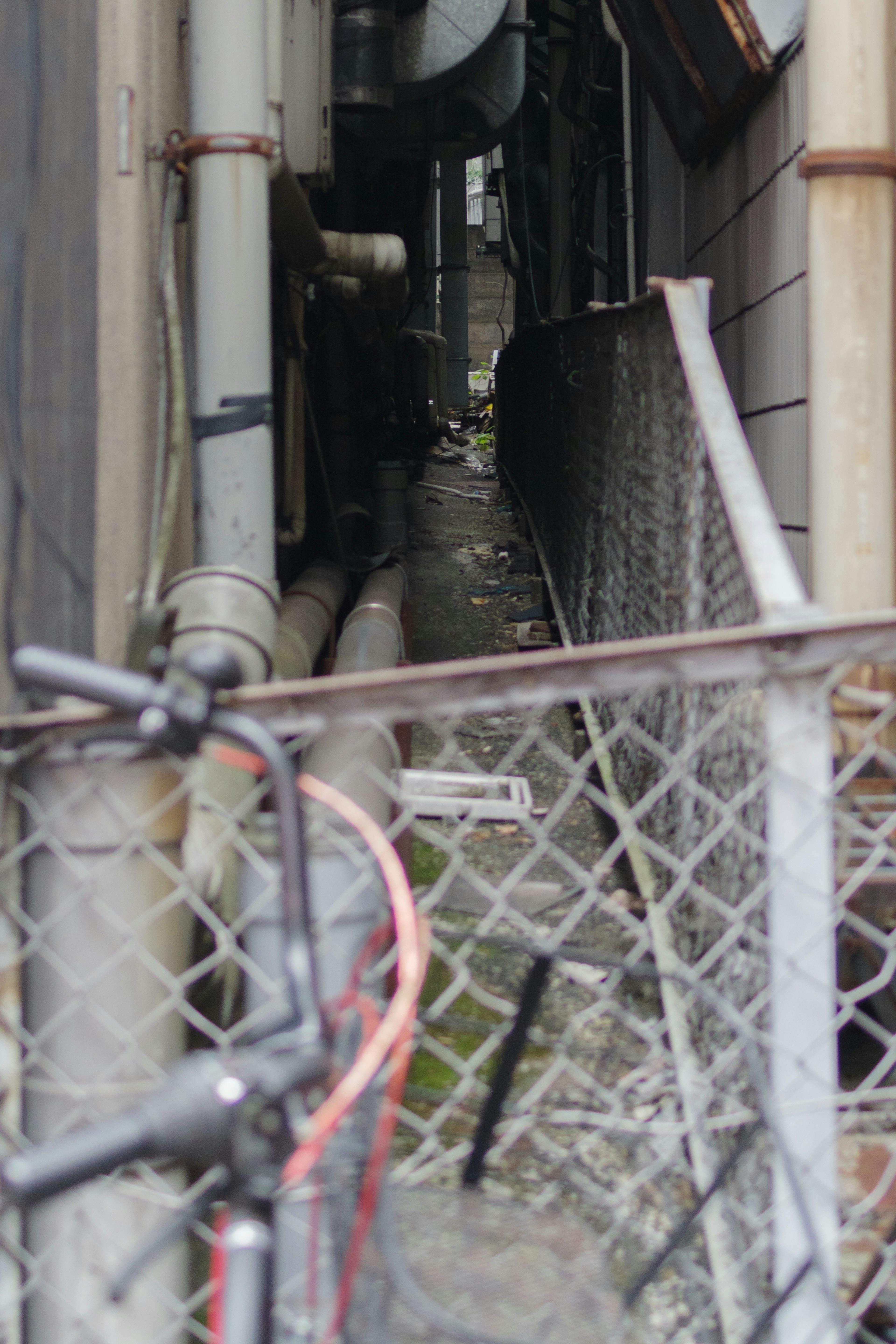 Callejón estrecho con cerca de metal y tuberías