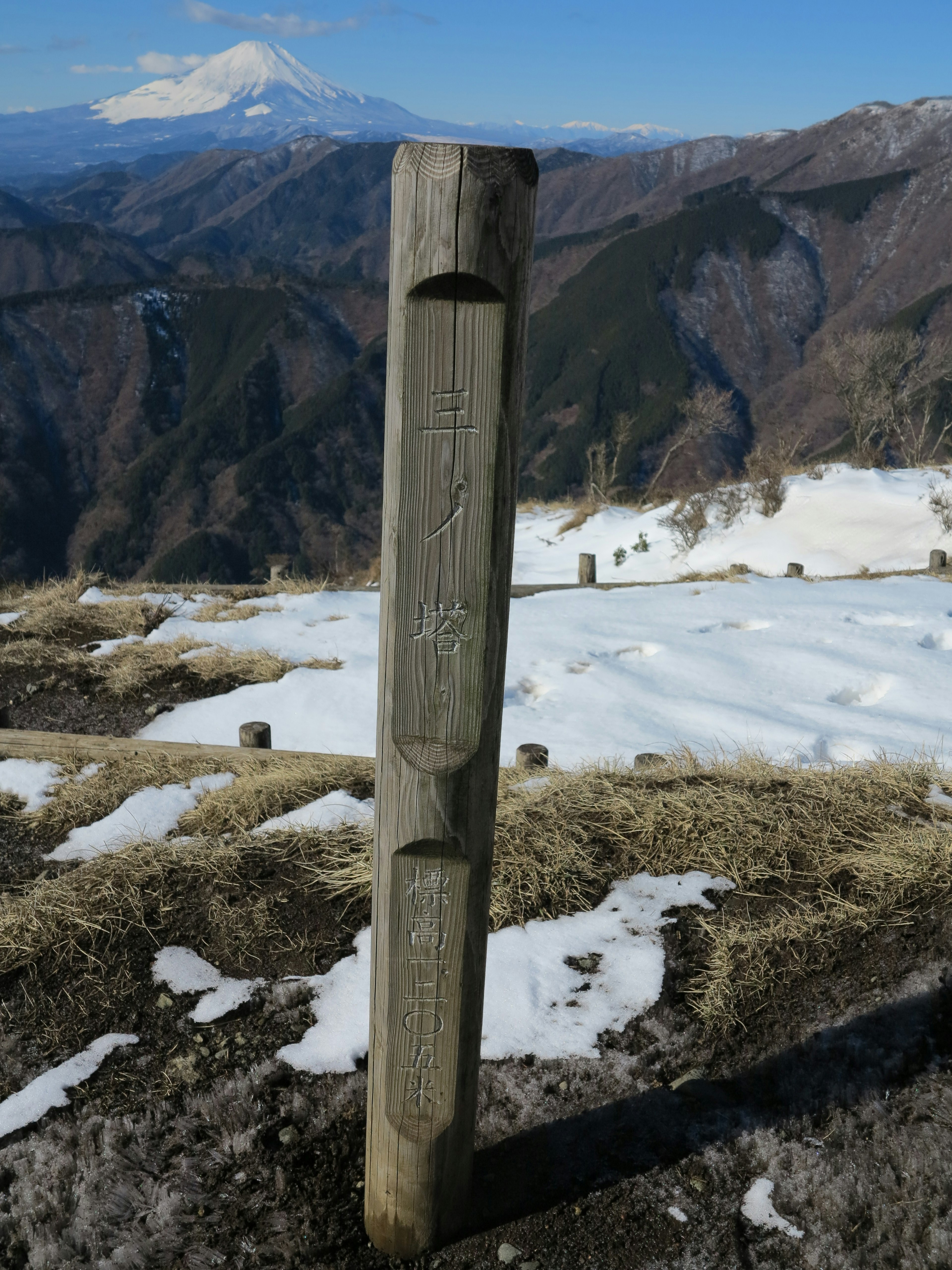 Palo di legno sulla cima della montagna con terreno coperto di neve e montagne lontane sullo sfondo