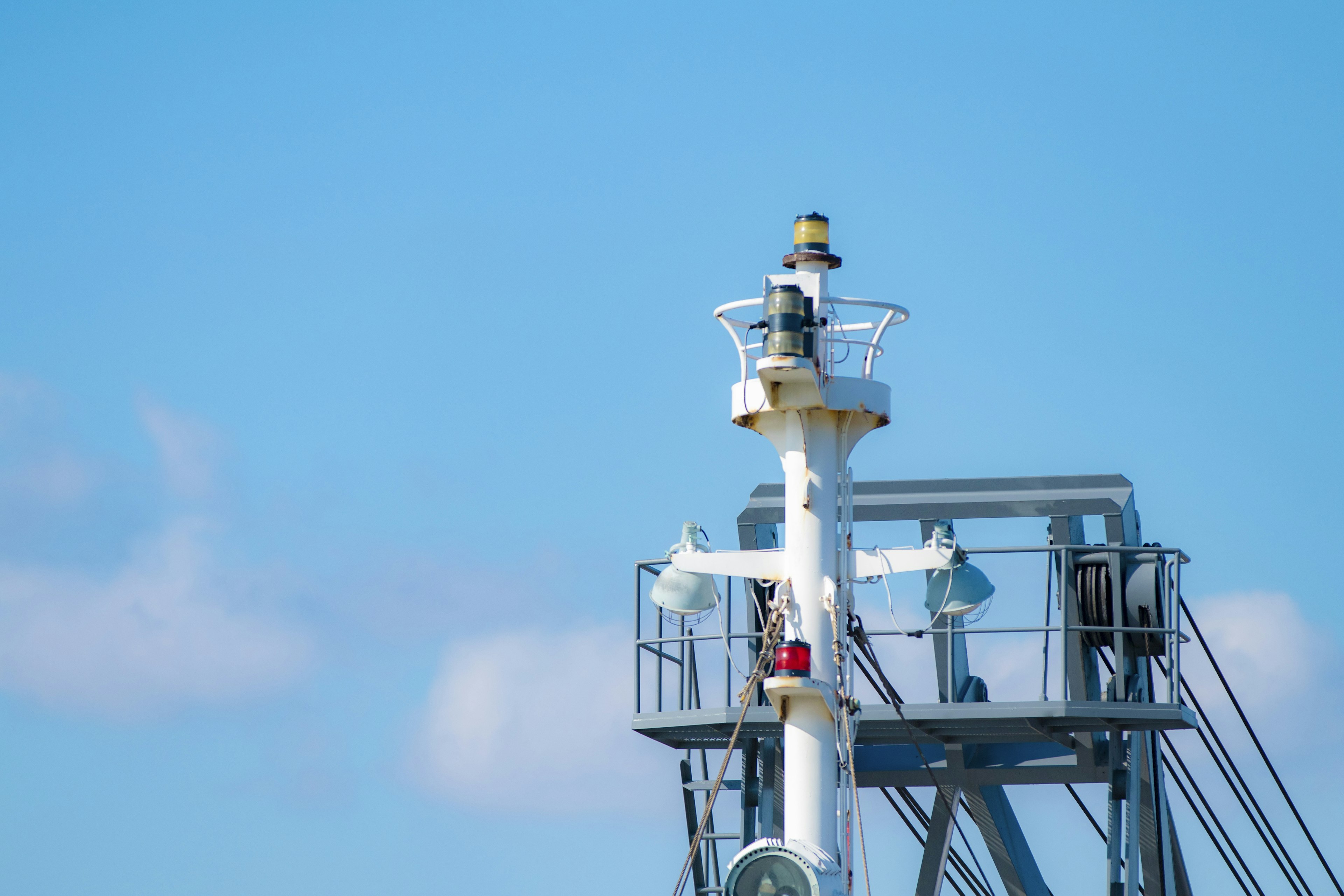 Part of a white lighthouse under a blue sky with surrounding structures