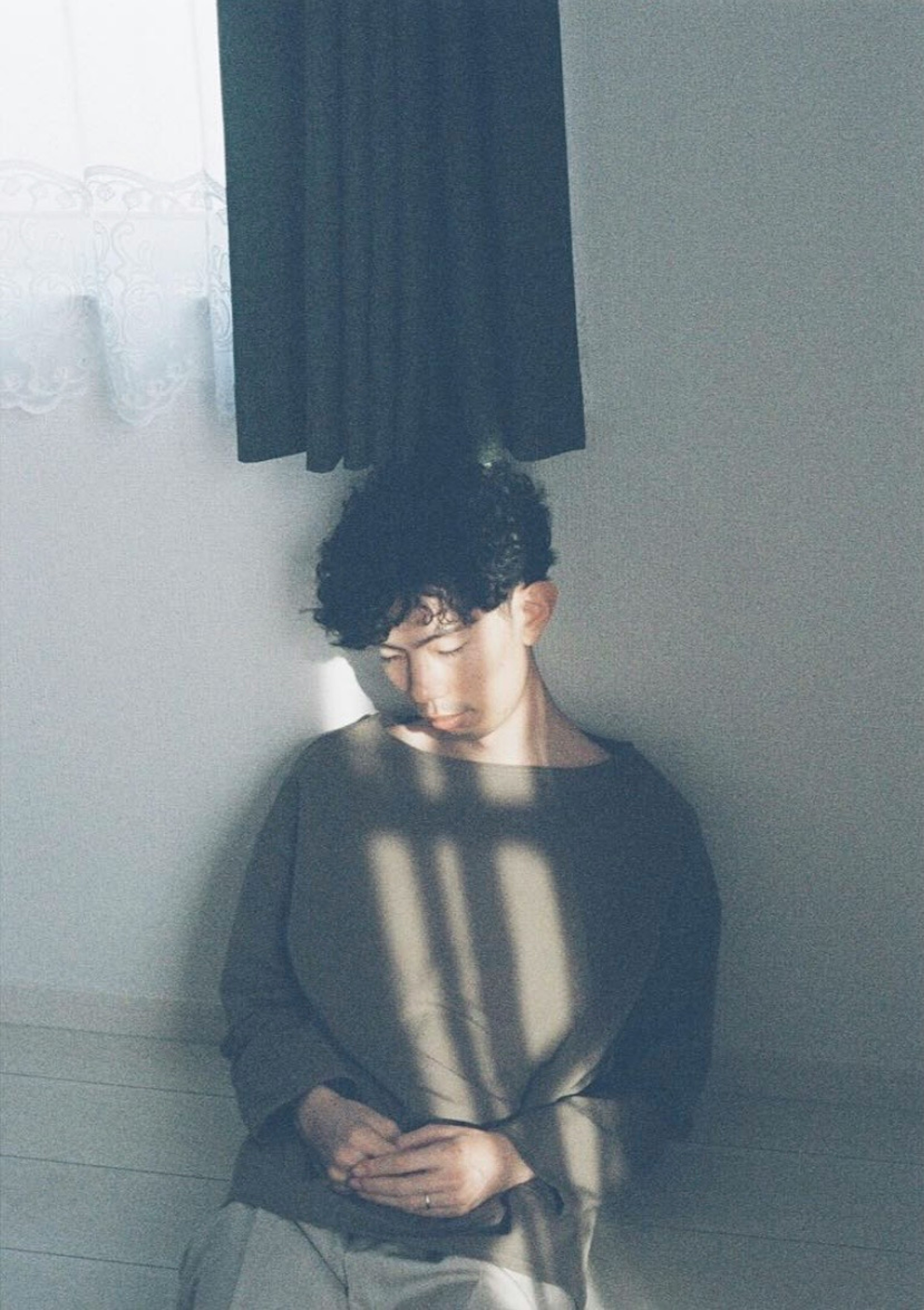 A young man leaning against a wall in soft light