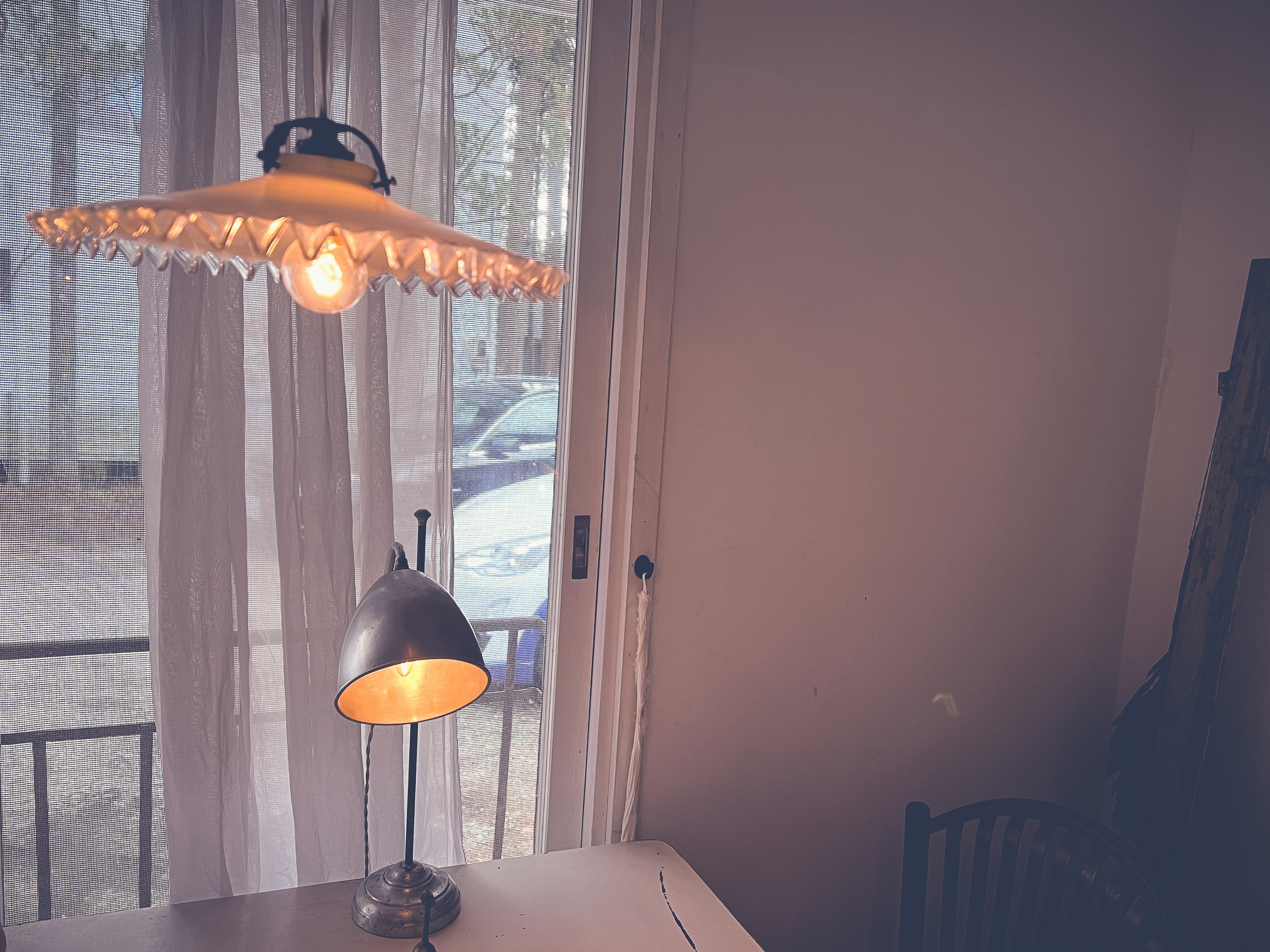 Lamp with a decorative shade and a metallic base near a window with sheer curtains