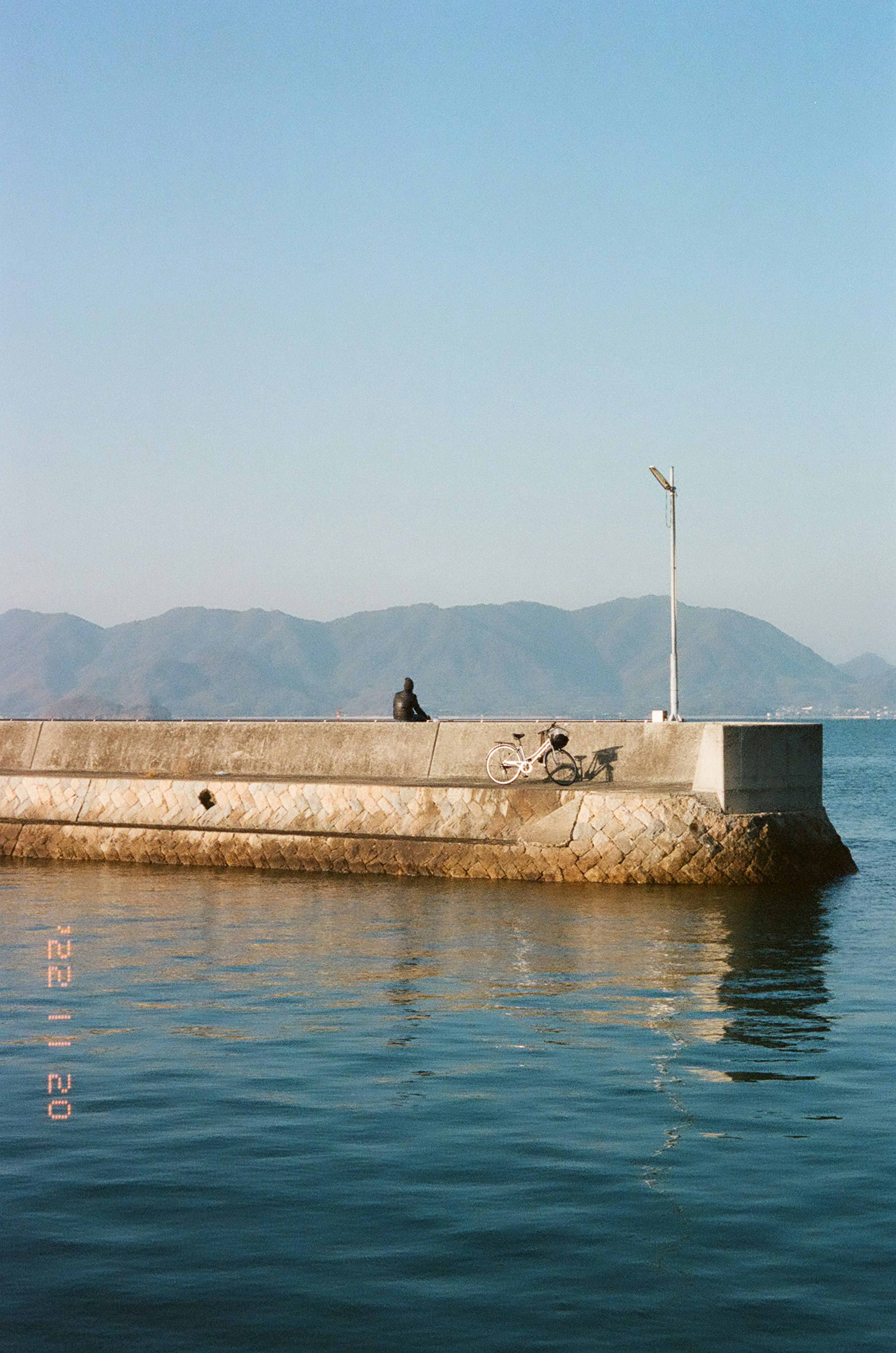 A person sitting on a pier overlooking calm waters and distant mountains