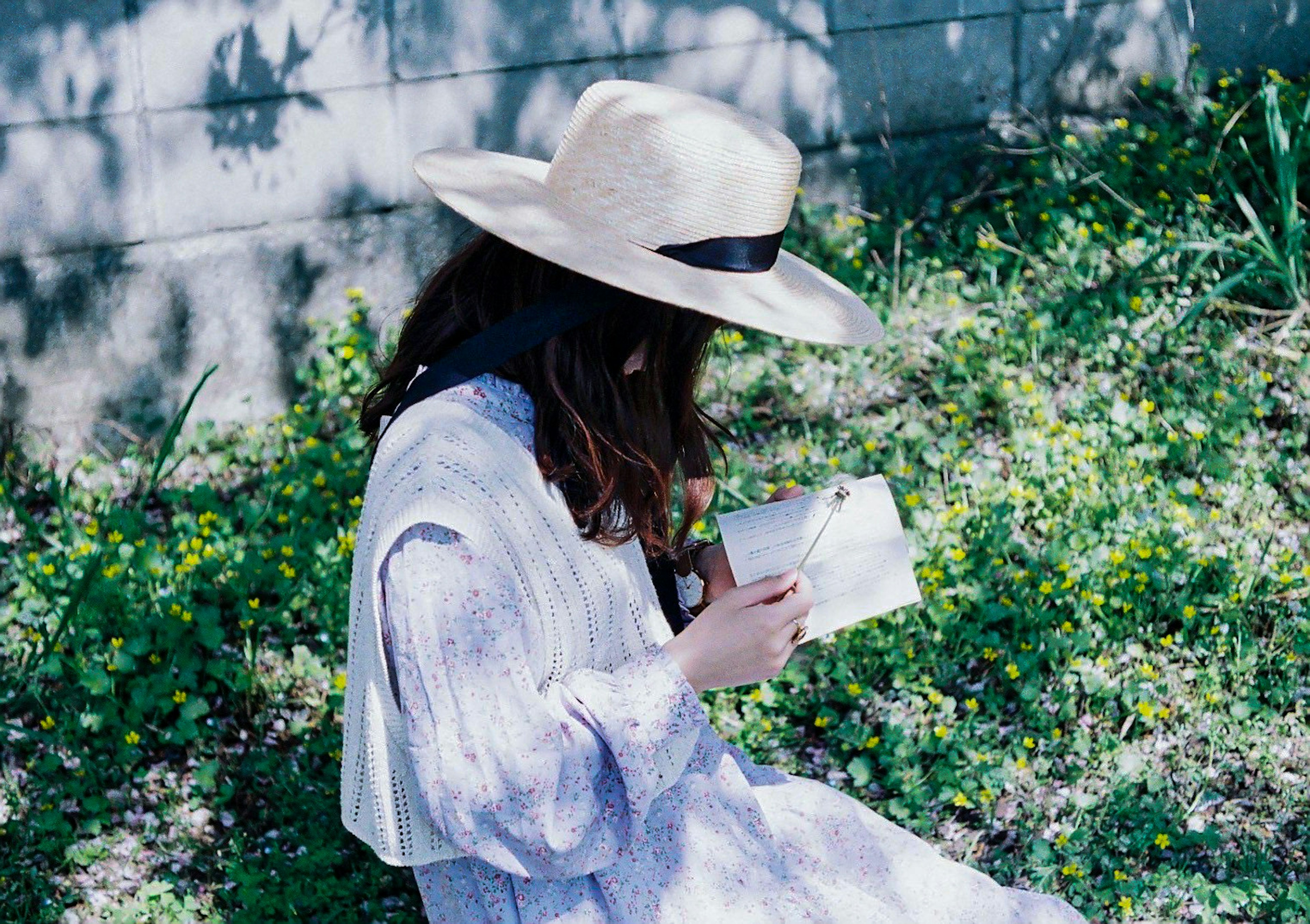 Donna seduta sull'erba che legge un libro indossando un grande cappello di sole