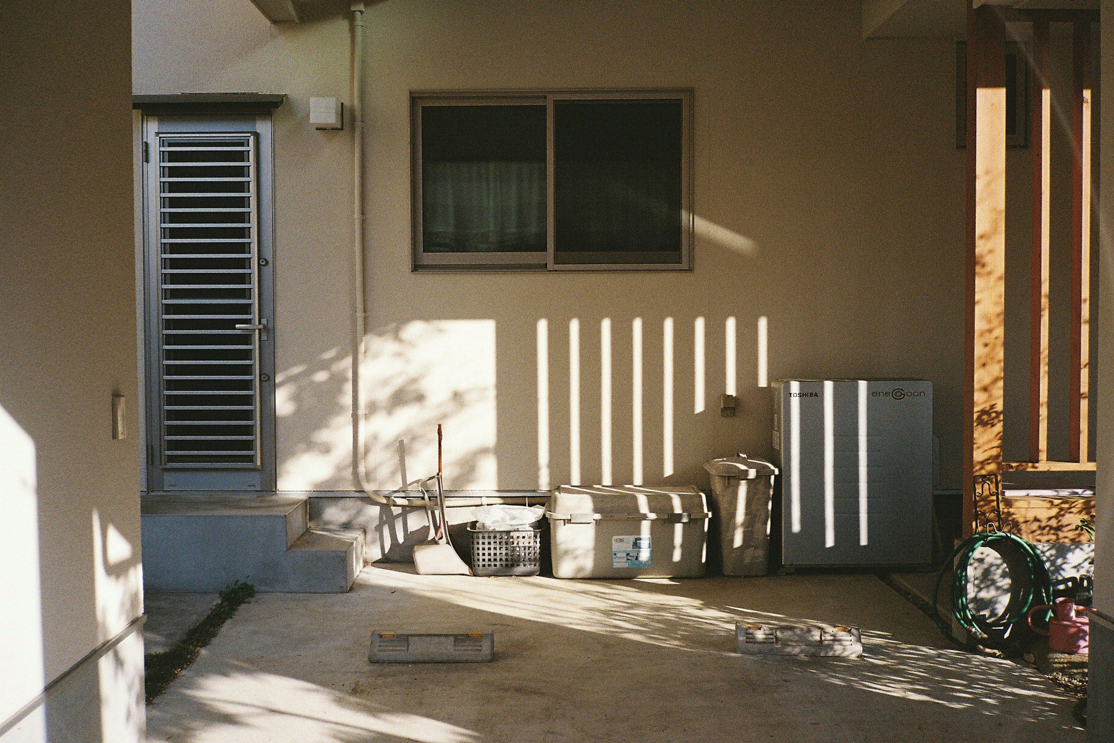 Foto di un angolo esterno di una casa con una finestra e una porta, ombre proiettate dalla luce del sole