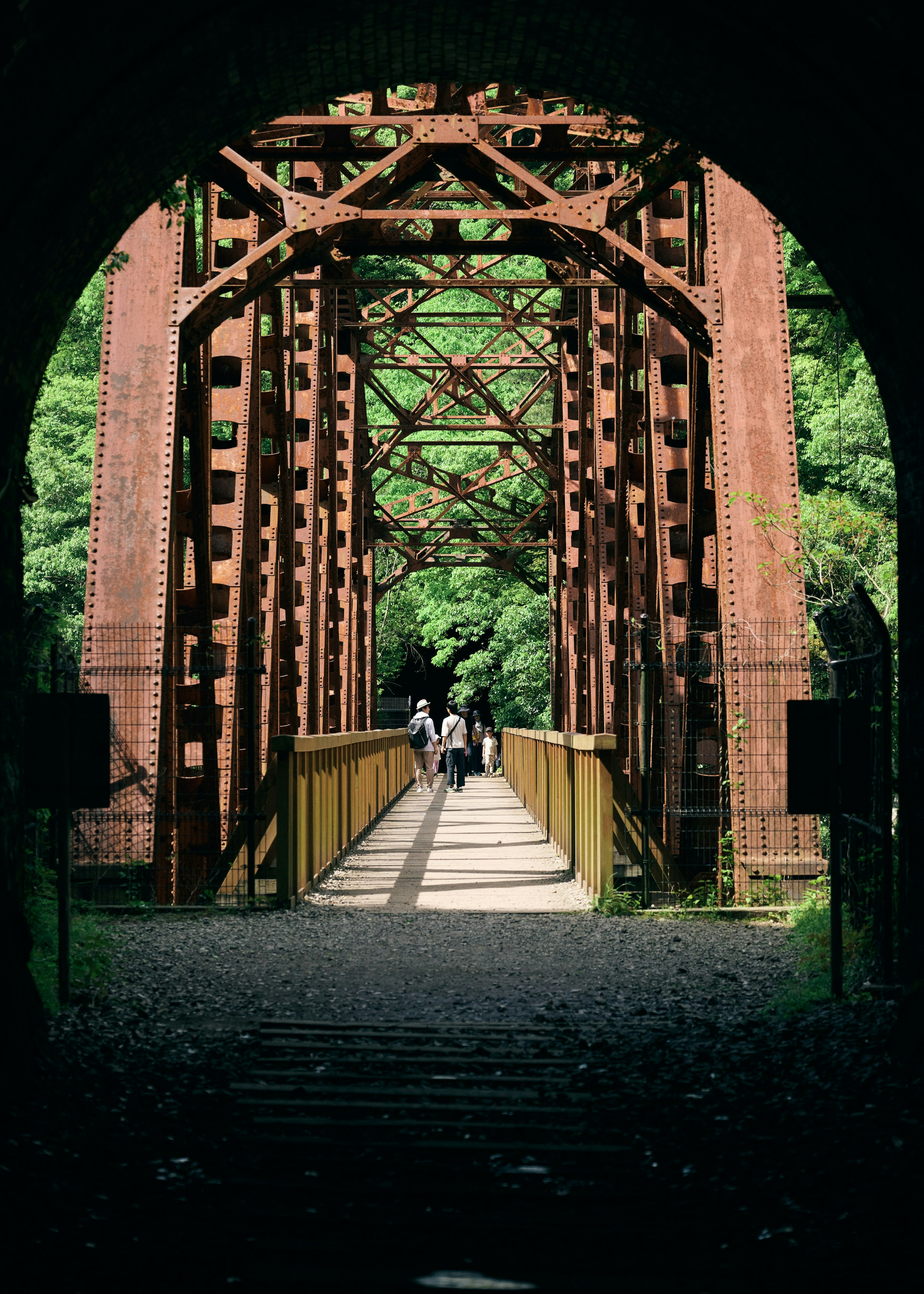 Red iron bridge with green foliage and people walking