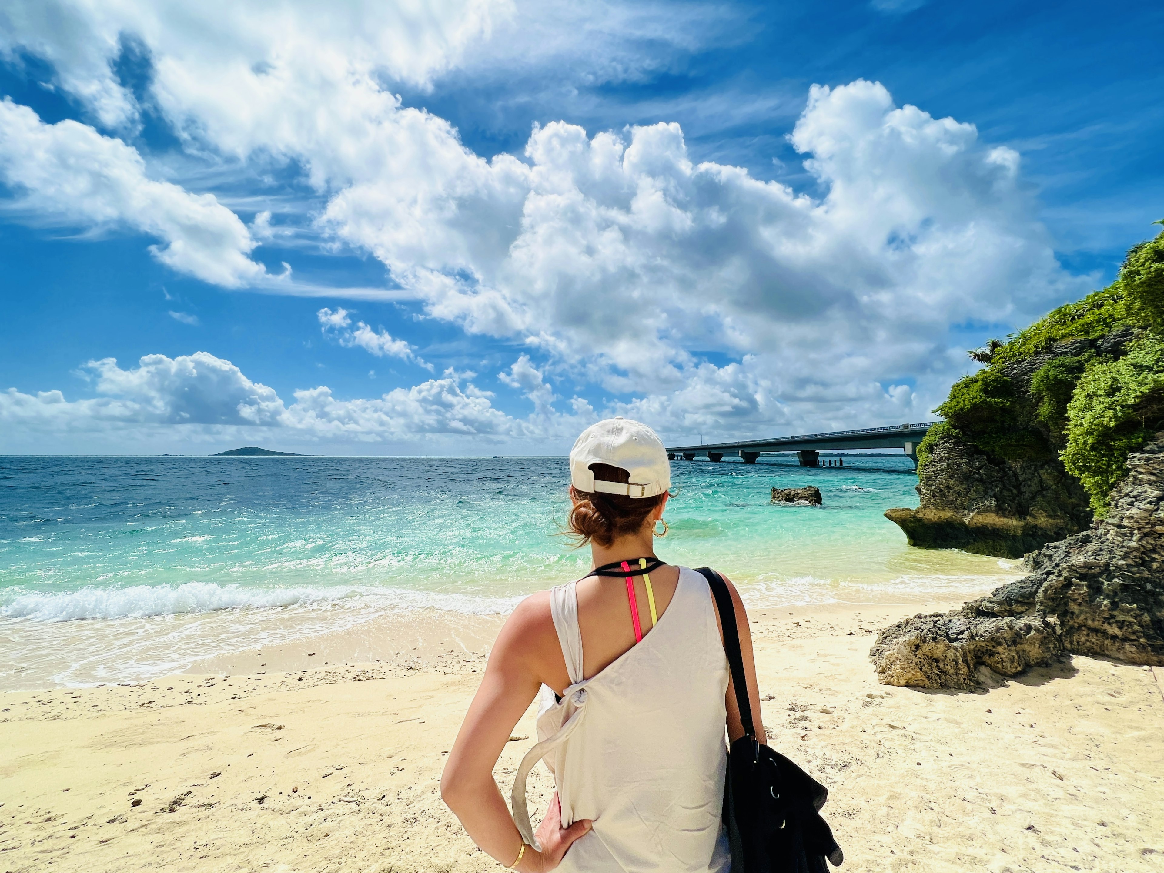 Perempuan menatap laut di pantai Langit biru dengan awan putih Jembatan terlihat di kejauhan