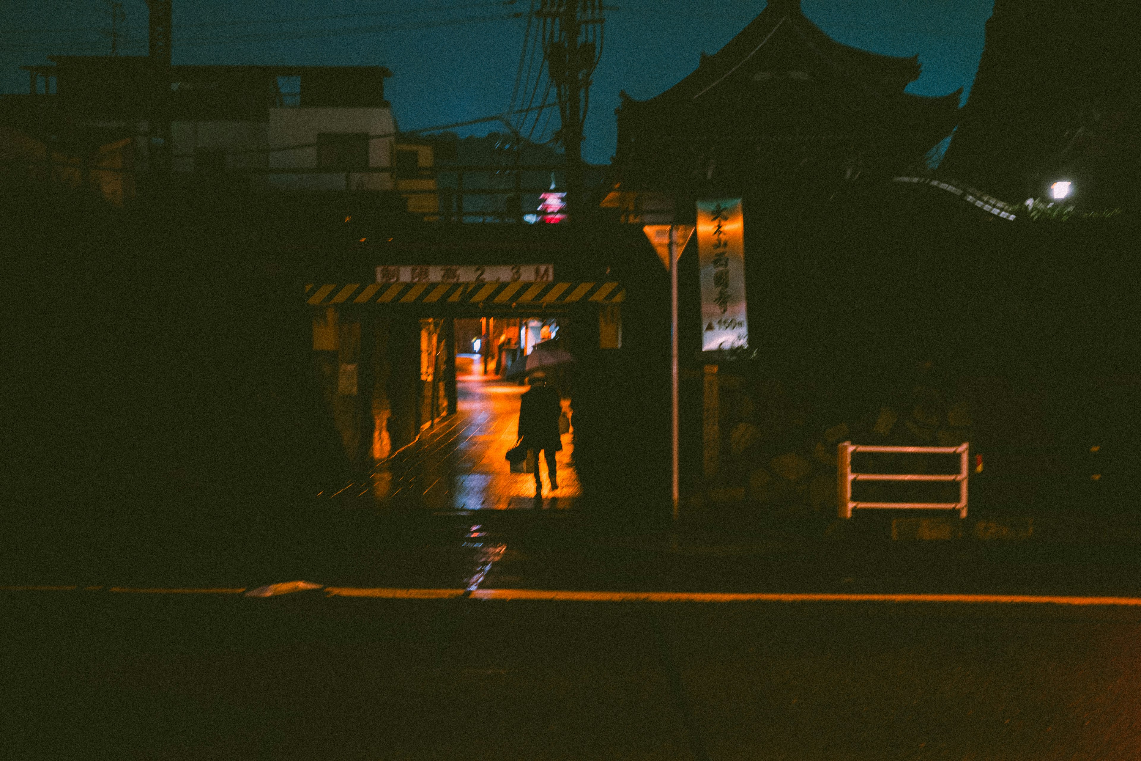 A person walking down a dimly lit street with warm lights and traditional architecture