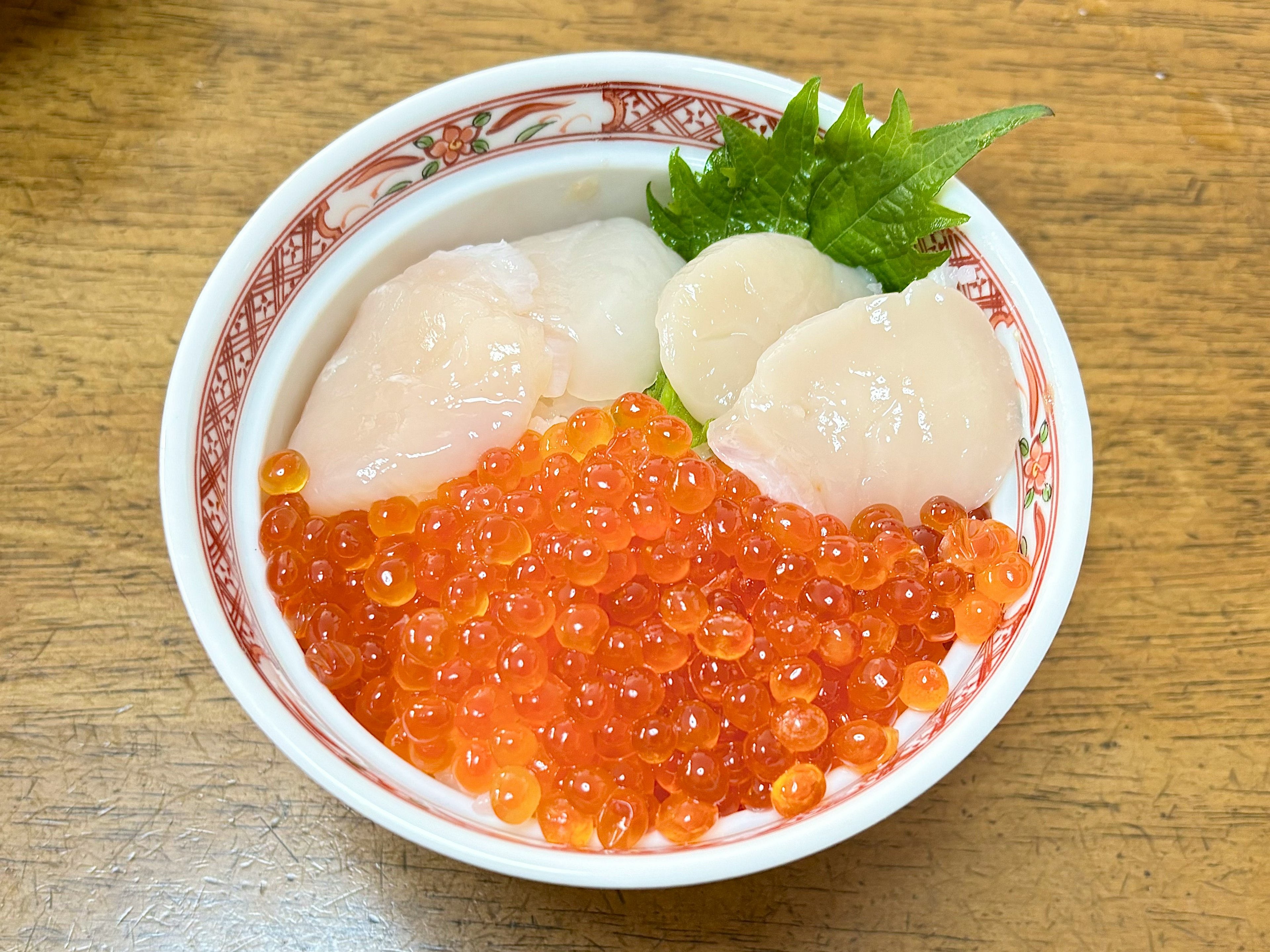 Un bol d'ikura vibrant et de pétoncles garni de feuilles de shiso