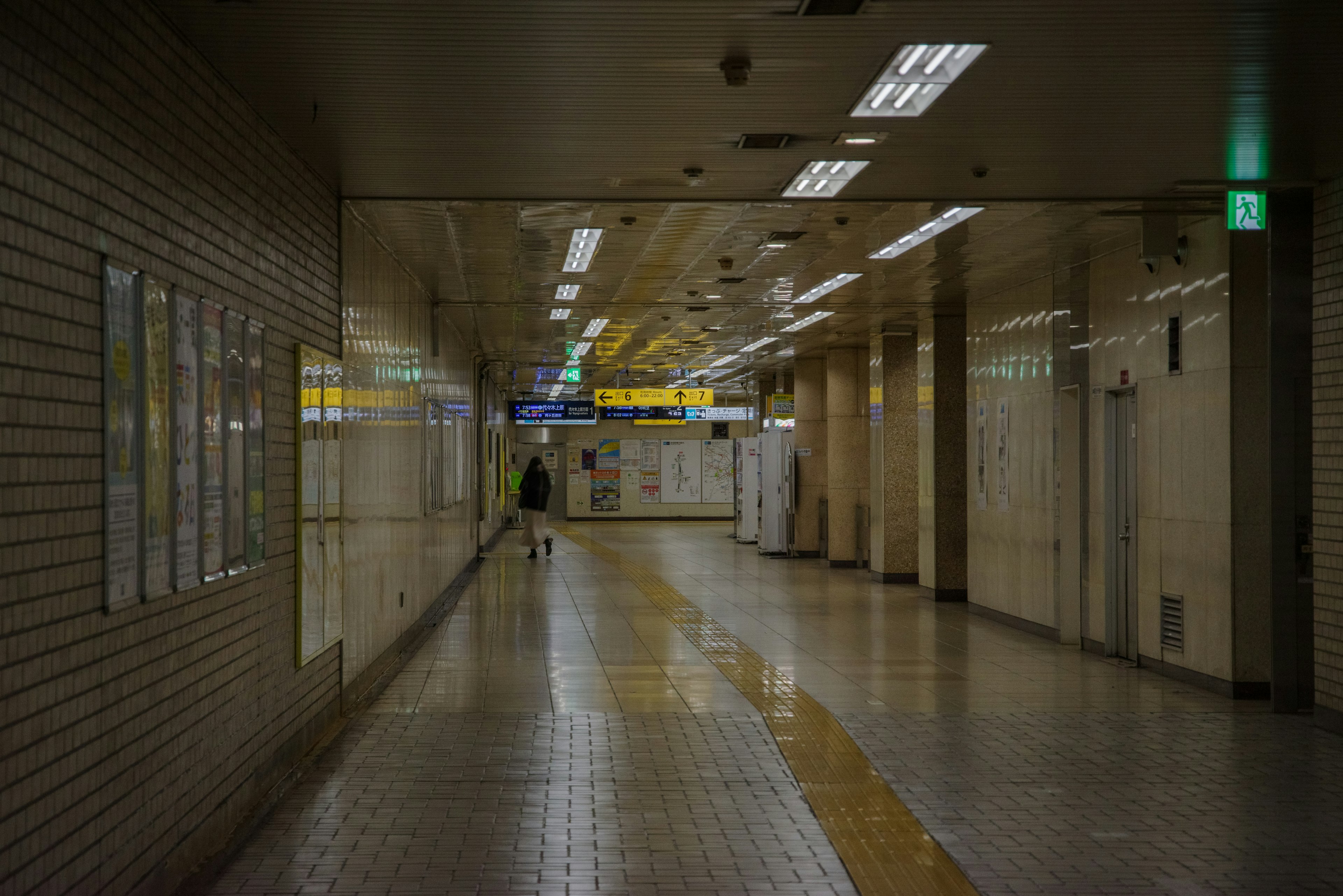 A dimly lit subway corridor with a lone person walking