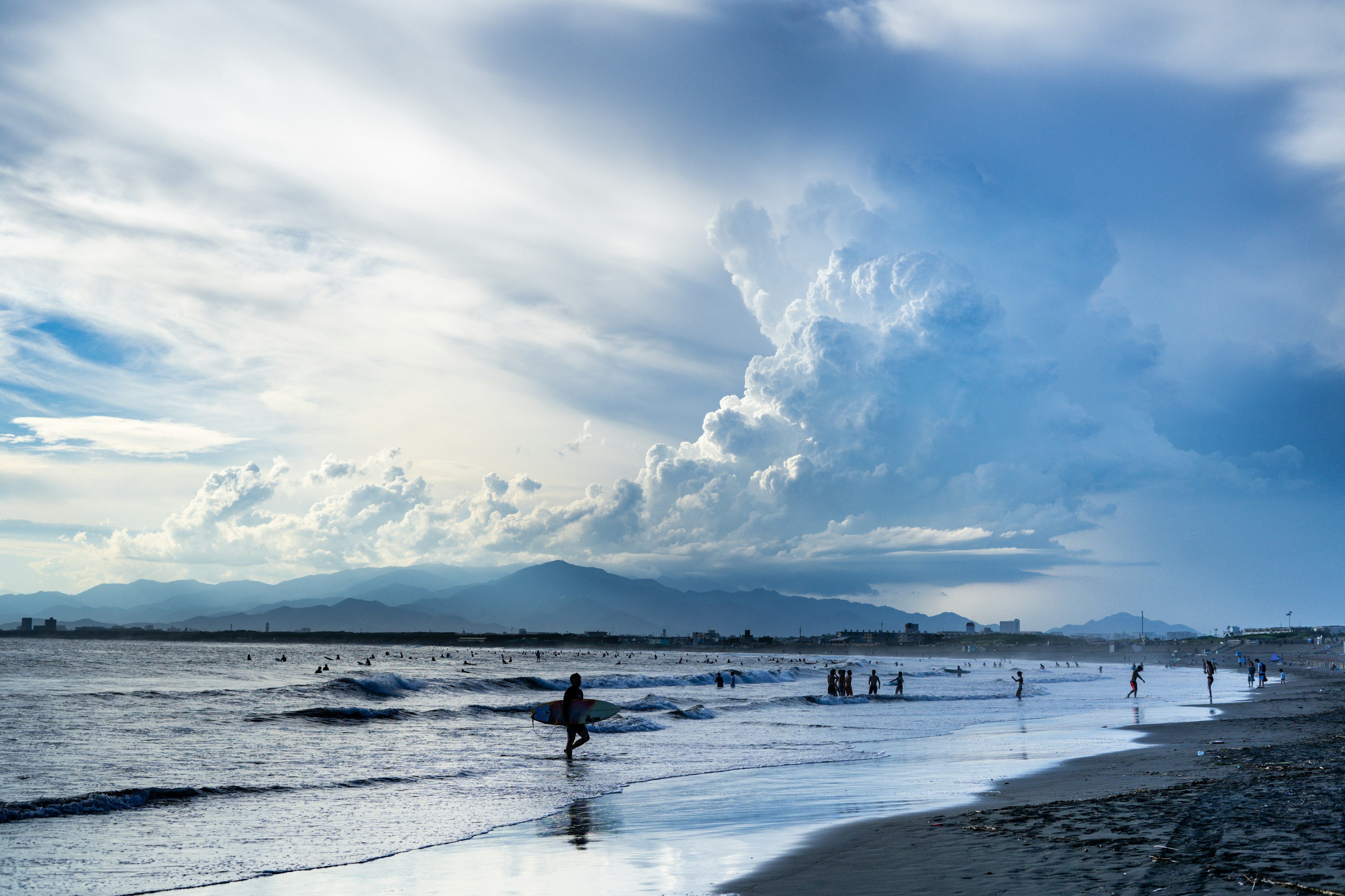 青い空と雲が広がる海辺の風景 砂浜を歩く人々と波