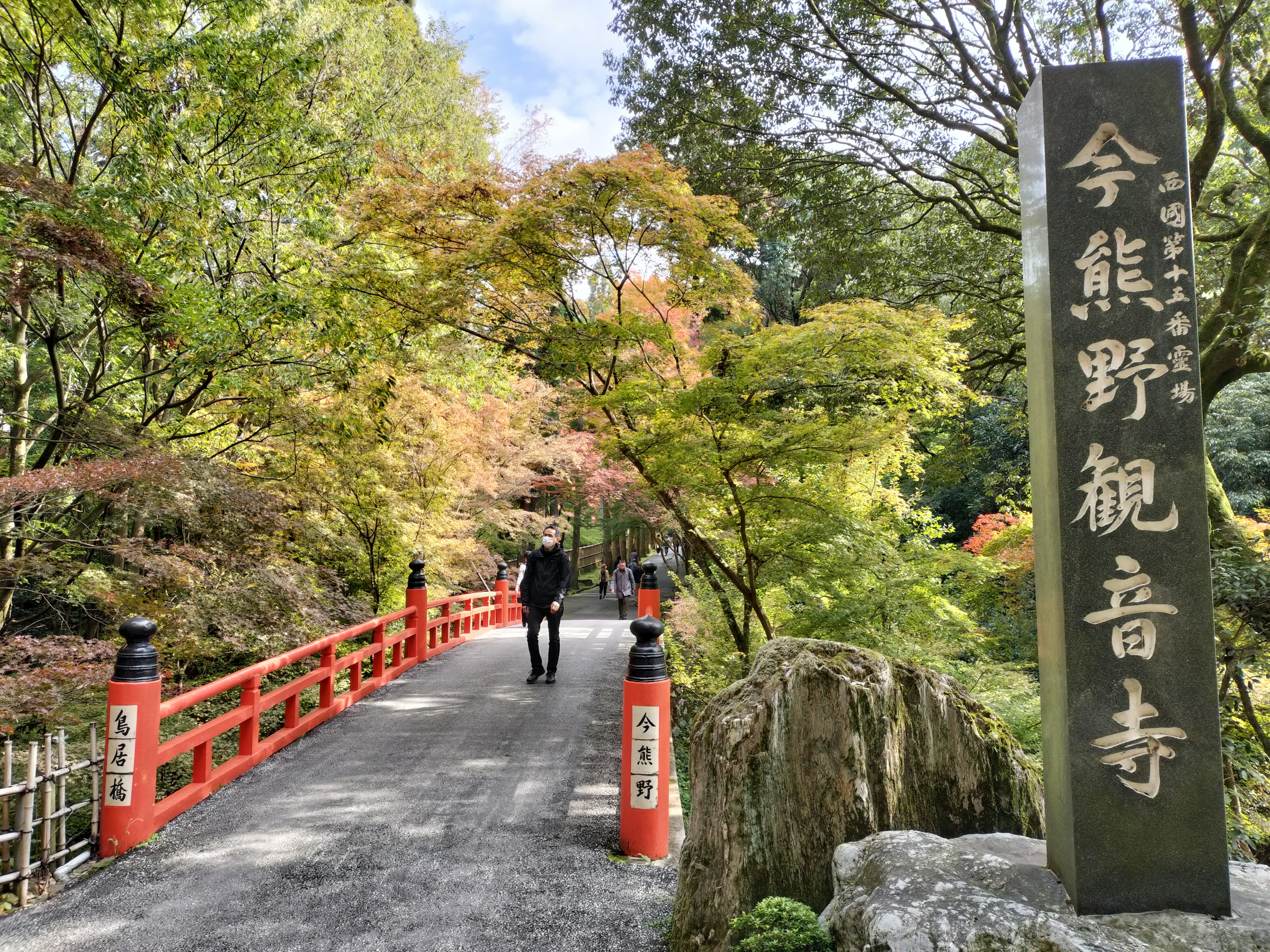 Pont rouge avec une verdure luxuriante menant au panneau du temple Kannon