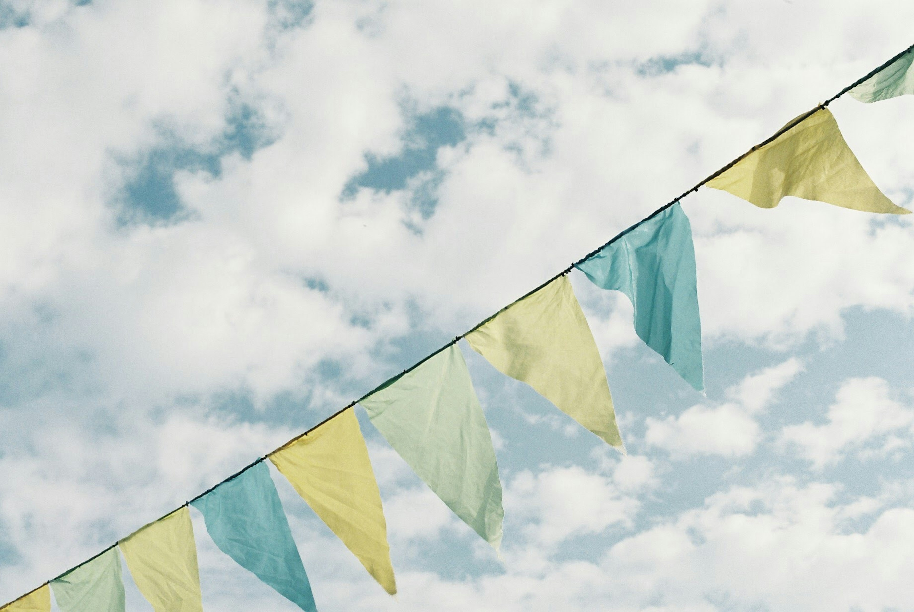 Bunte Fahnen hängen vor einem Hintergrund aus blauem Himmel und weißen Wolken