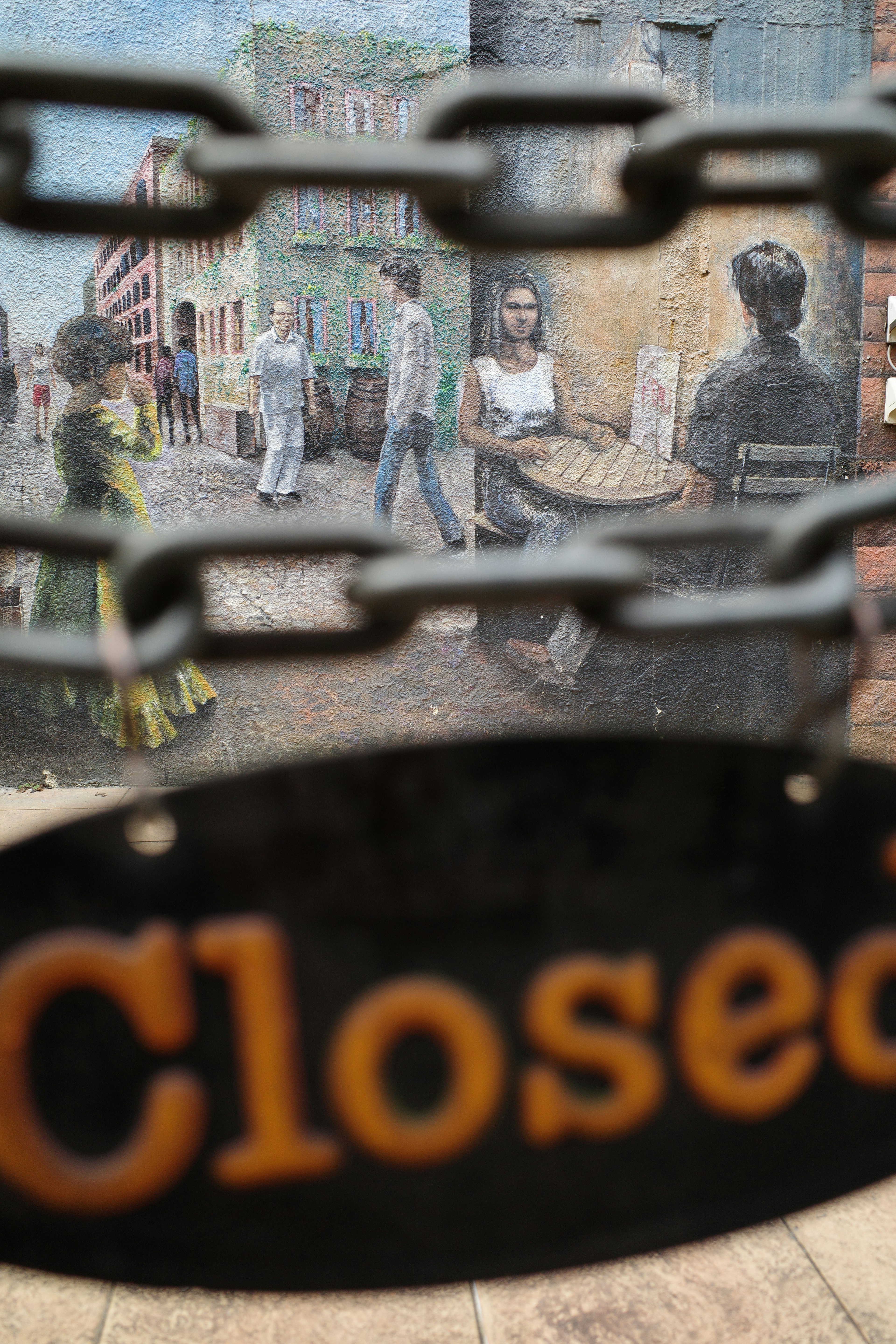 A 'Closed' sign hanging on a chain in front of a painted street scene