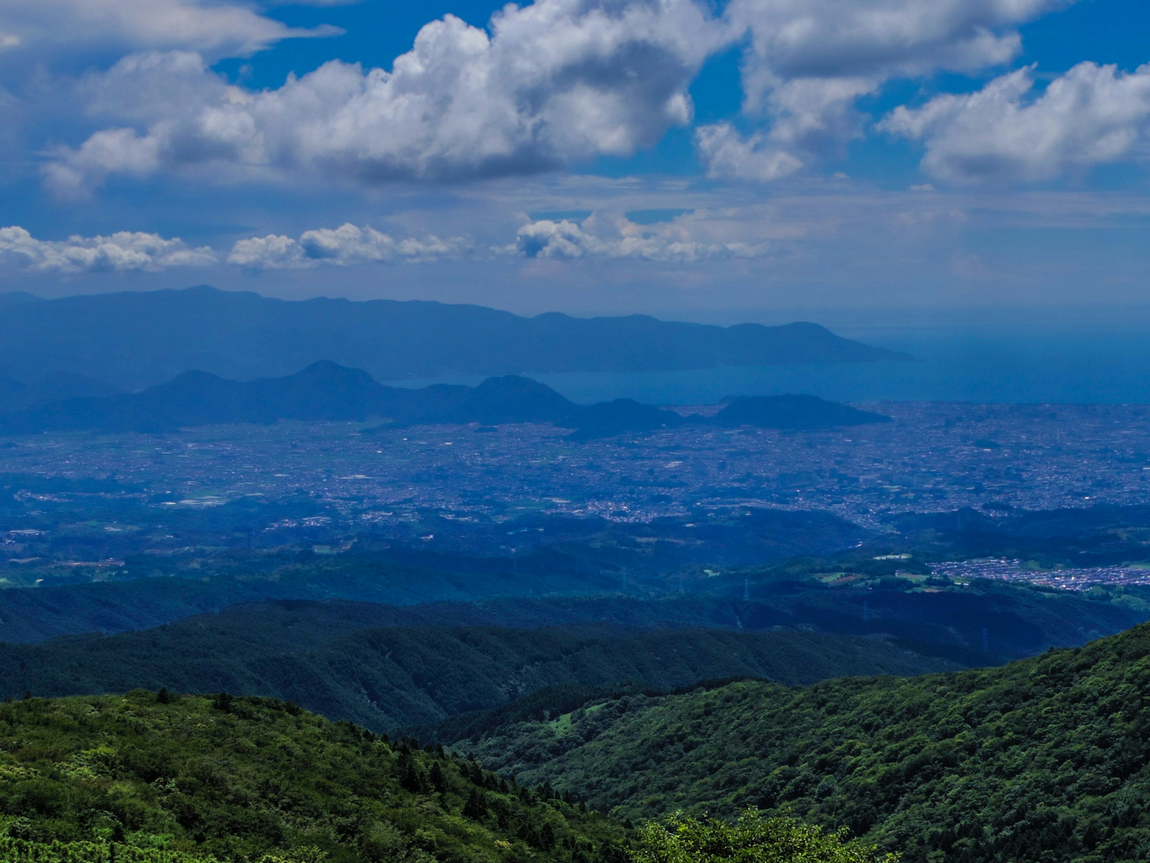 Paisaje montañoso con cielo azul y nubes colinas verdes y paisaje urbano distante