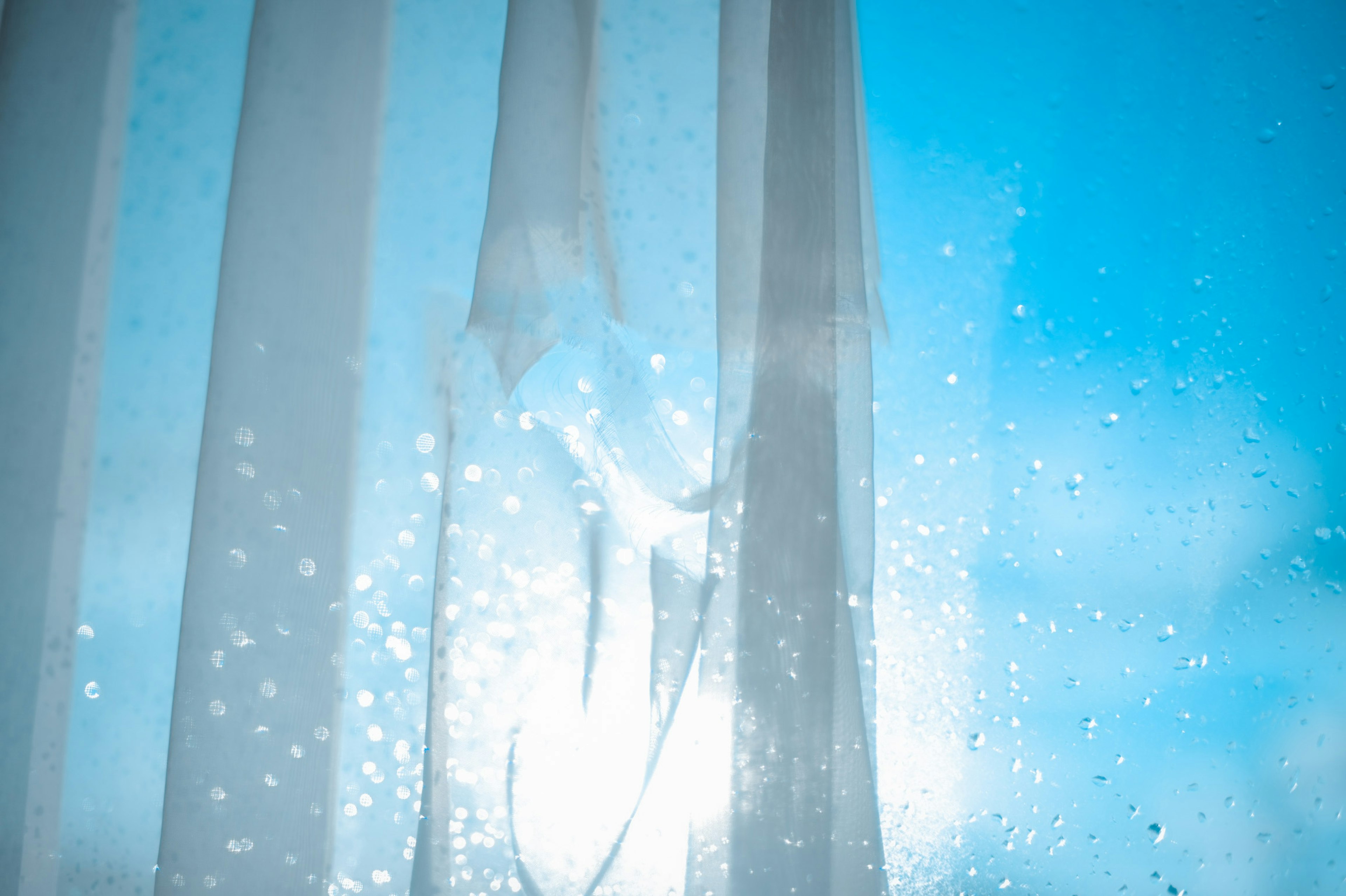 Una vista di tende bianche trasparenti con gocce d'acqua contro un cielo blu