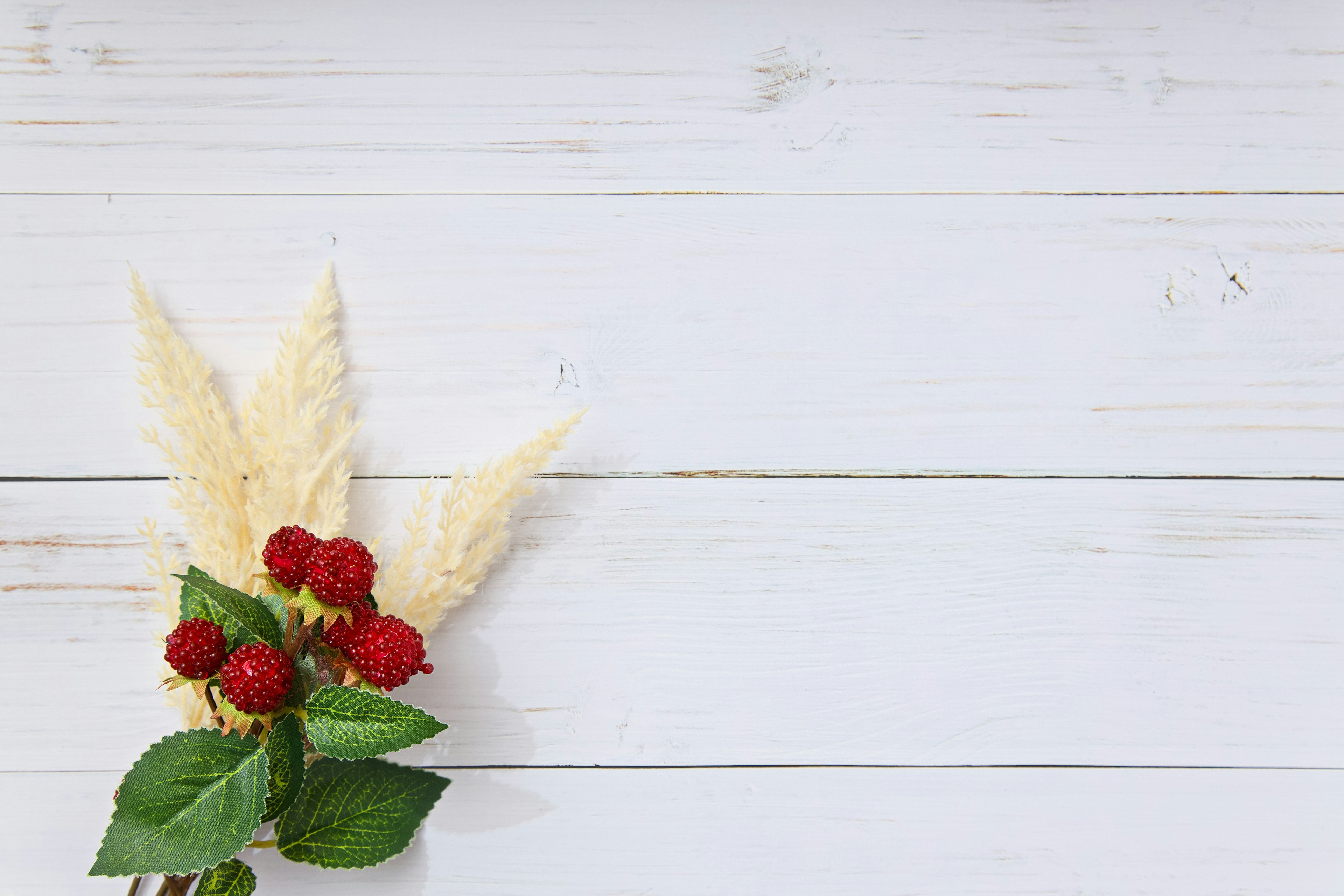 Arrangement of red raspberries and green leaves on a white wooden background