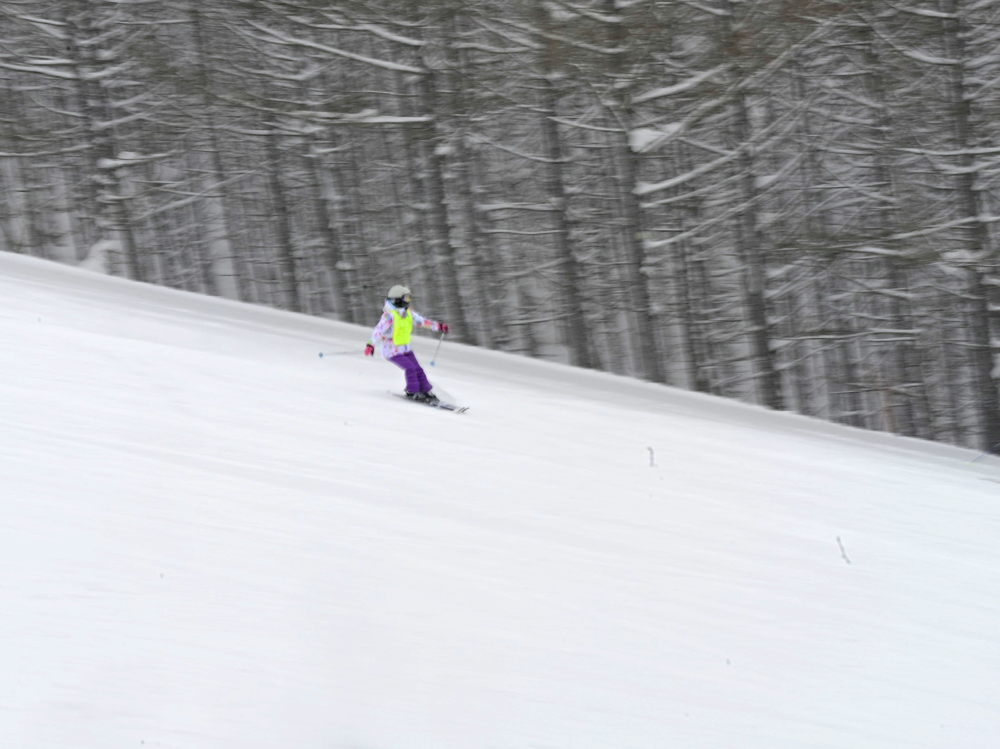 Skier gliding down a snowy slope with trees in the background