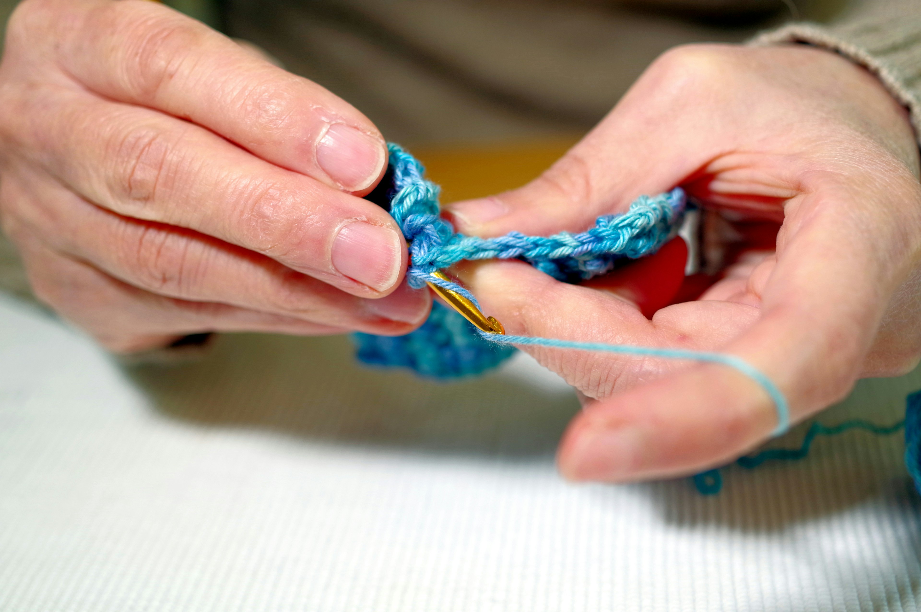 Gros plan sur des mains en train de crocheter avec du fil bleu