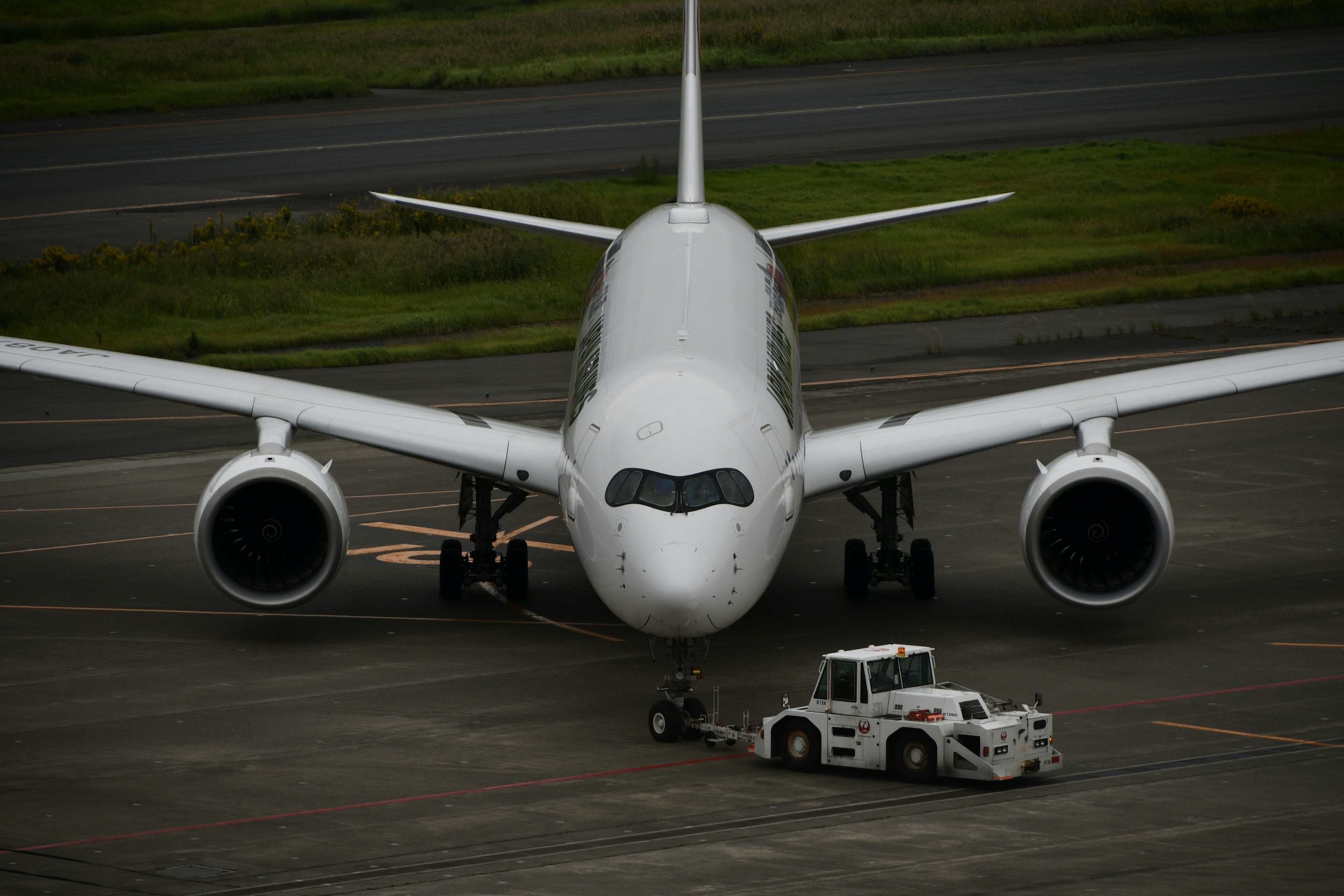 Ein weißes Passagierflugzeug, das auf der Startbahn geparkt ist, mit einem Abschlepptraktor davor