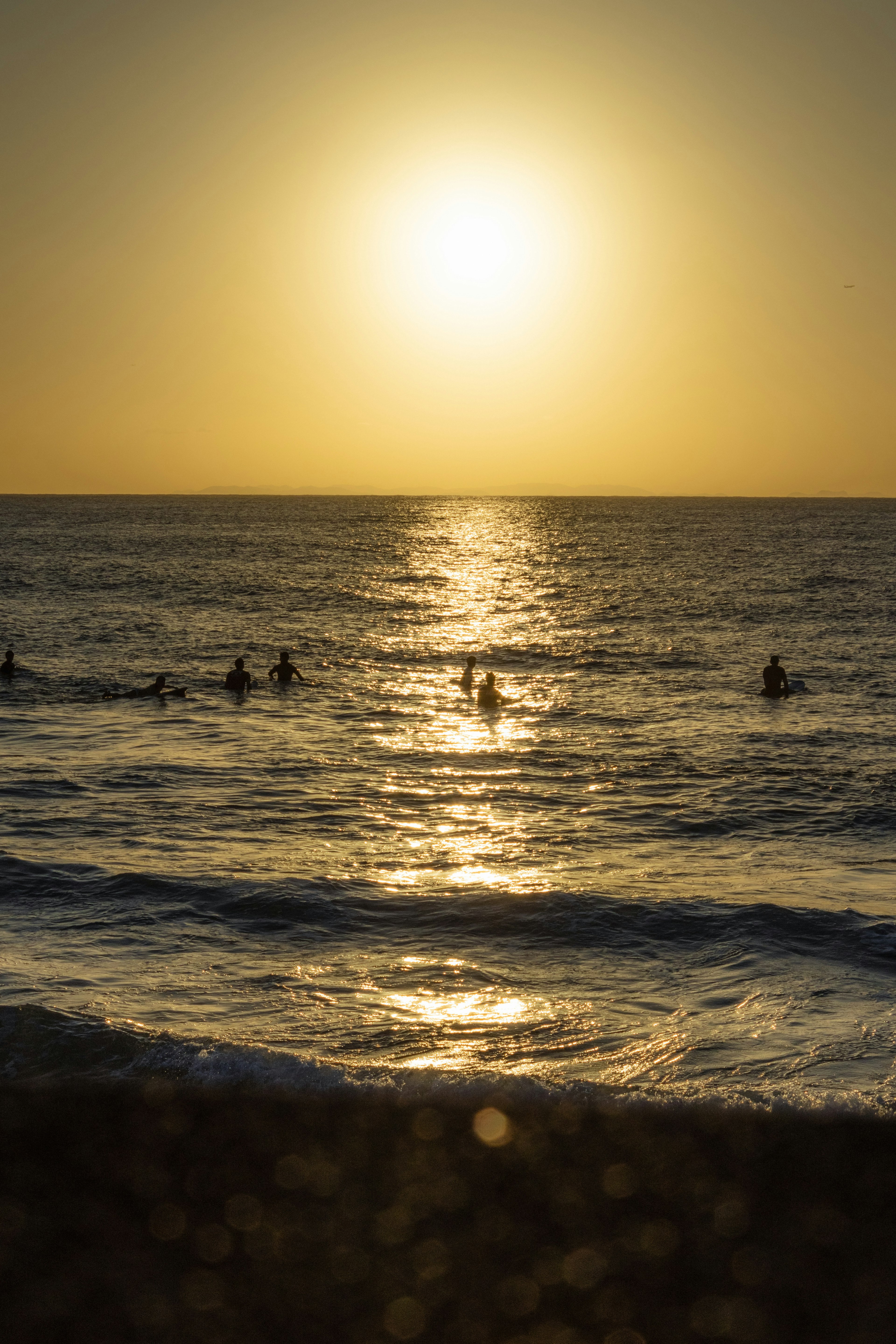 海でサーフィンをする人々と夕日のシルエット