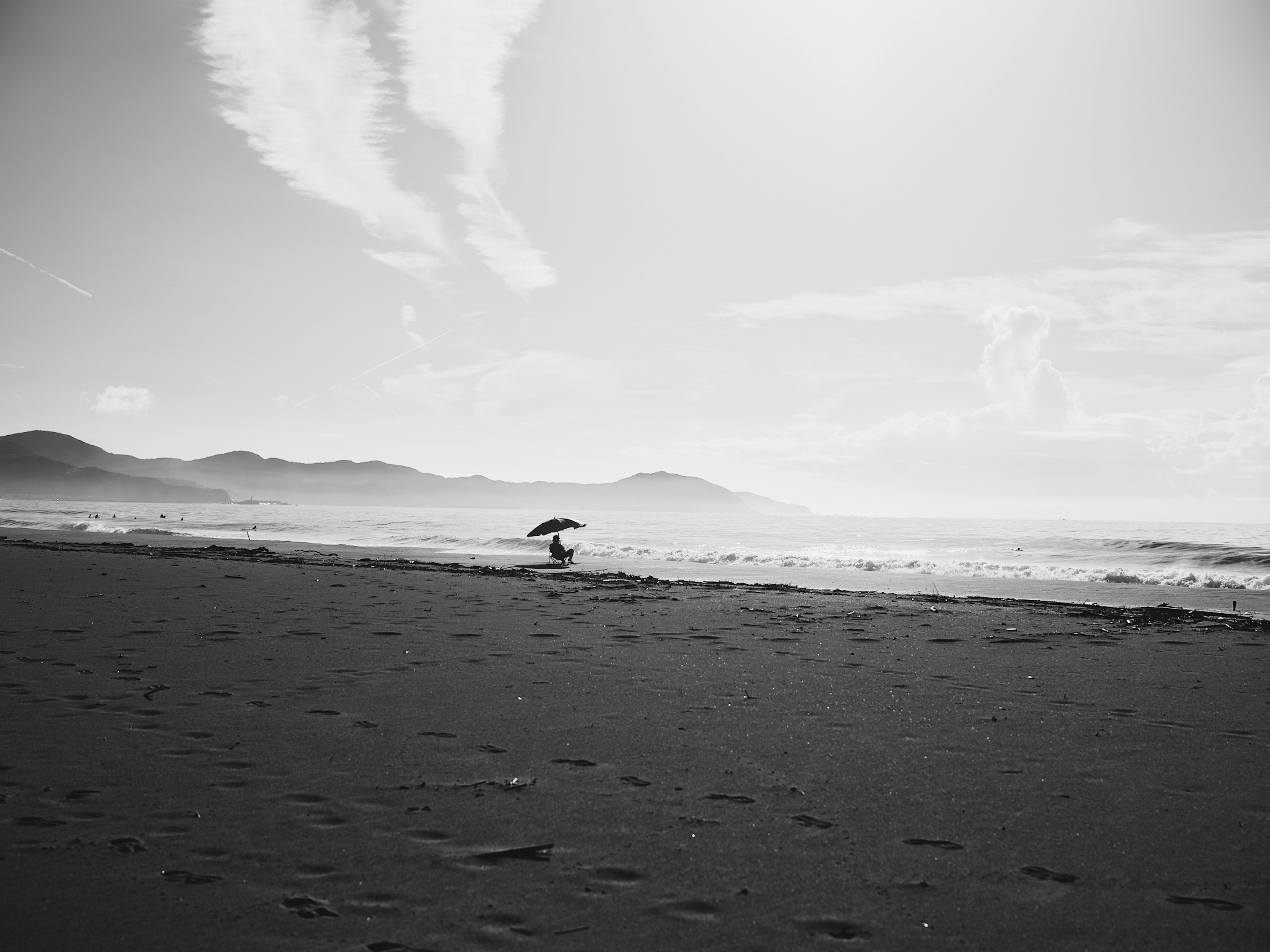 黑白海滩场景，有一个撑伞的人和波浪