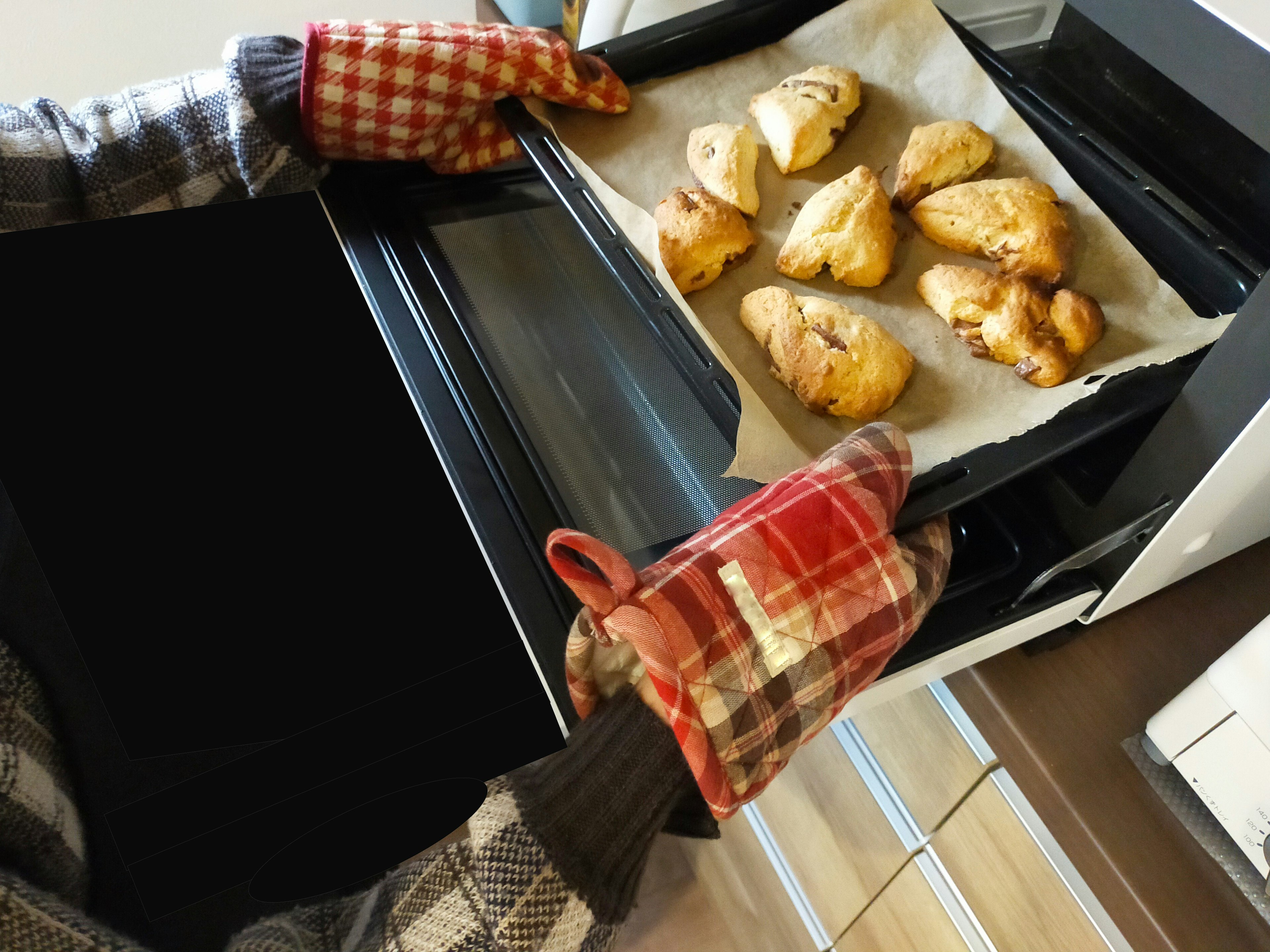 Hands removing freshly baked cookies from the oven