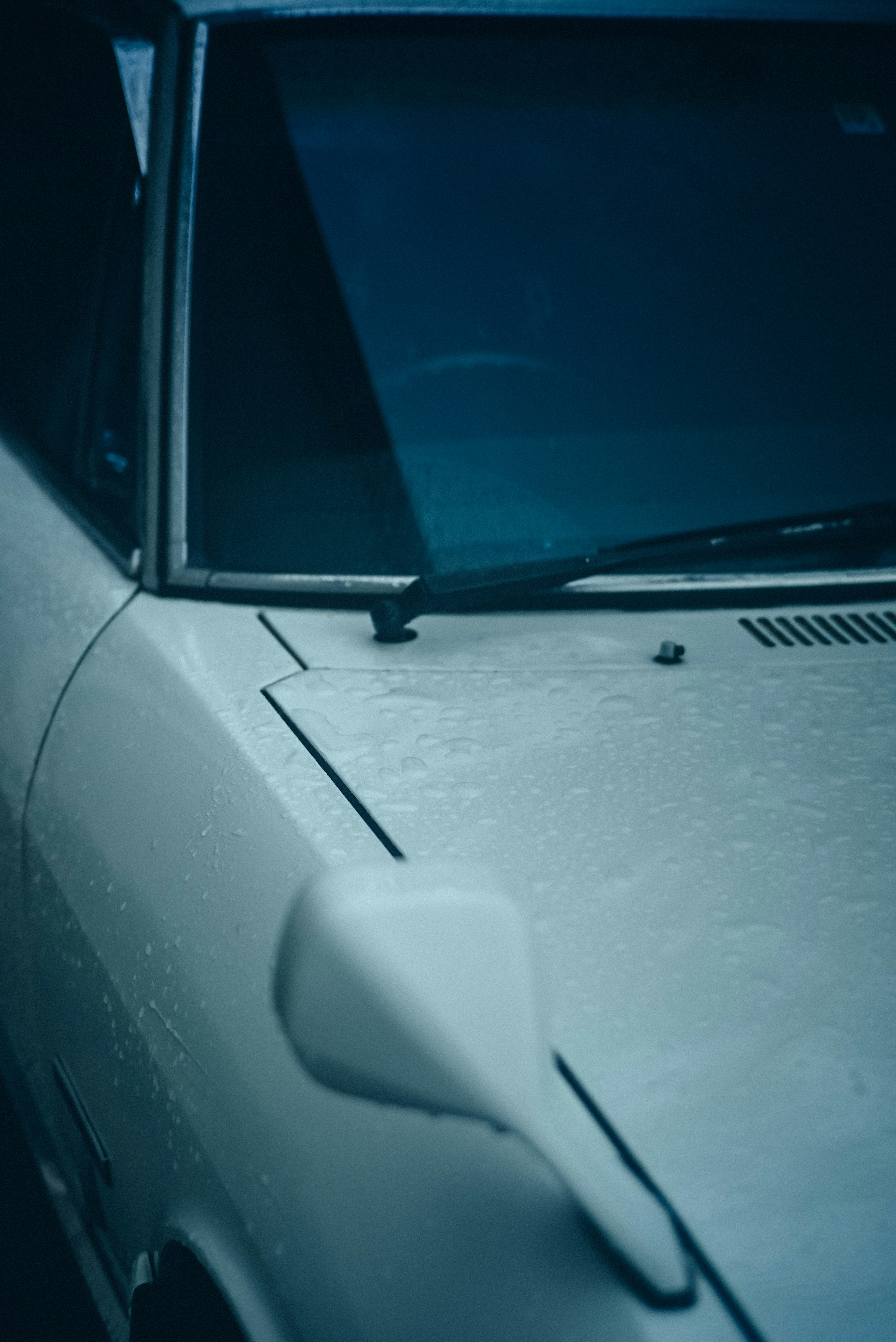 雨水覆蓋的白色汽車引擎蓋和擋風玻璃特寫