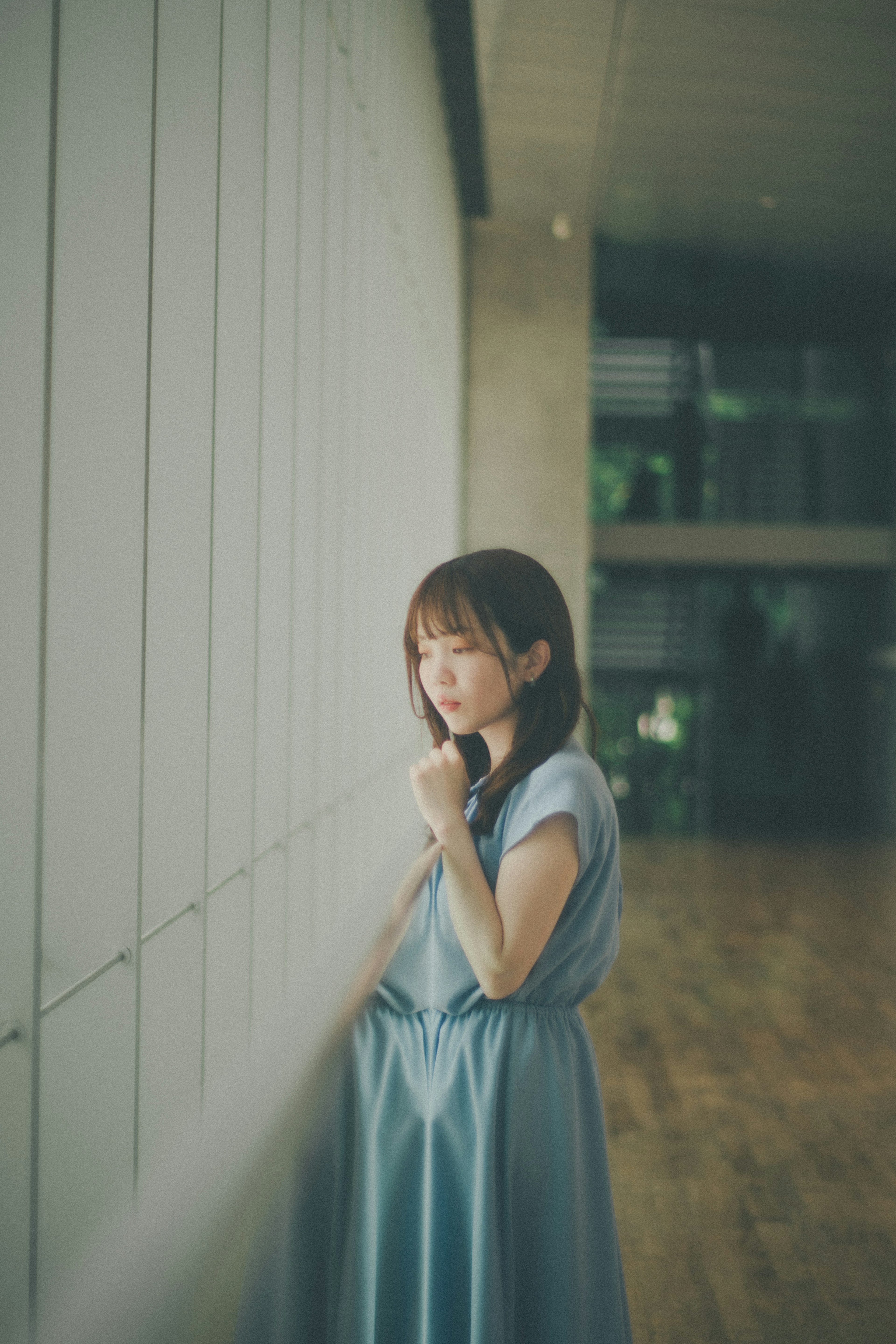 A woman in a blue dress standing by a window deep in thought