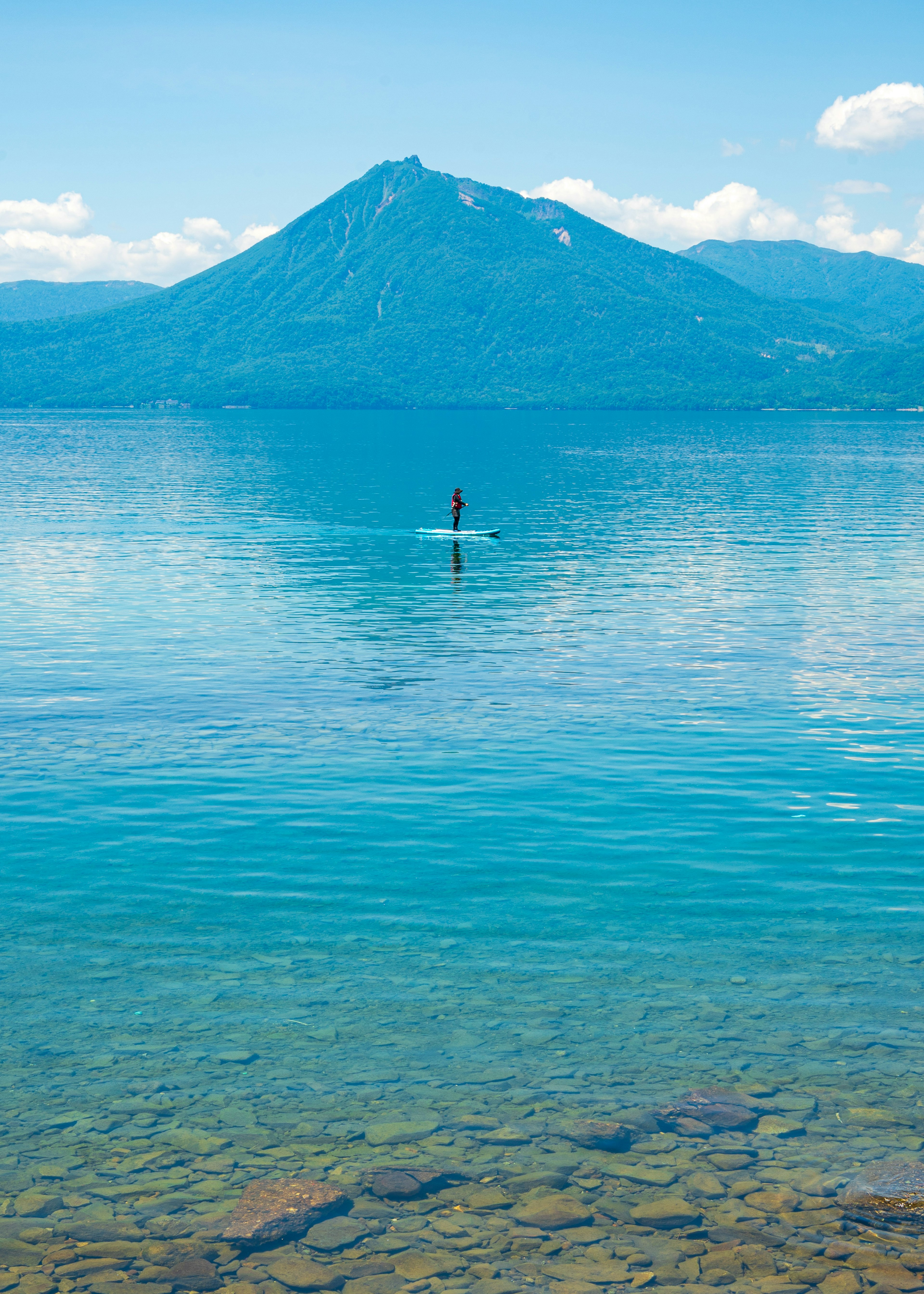 青い湖の上でパドルボードを楽しむ人と背景にそびえる山