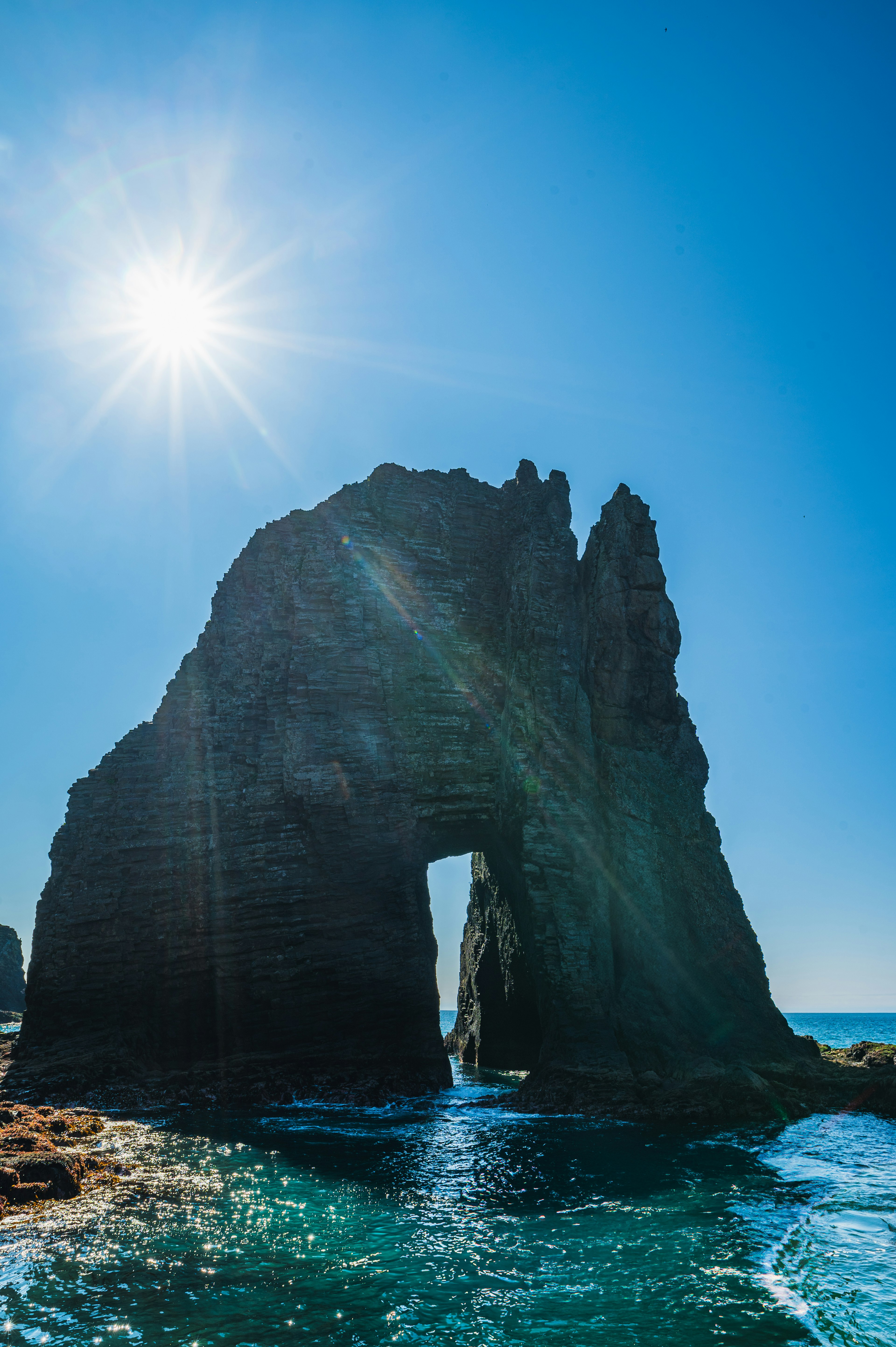 海の近くに立つ大きな岩のアーチと明るい太陽