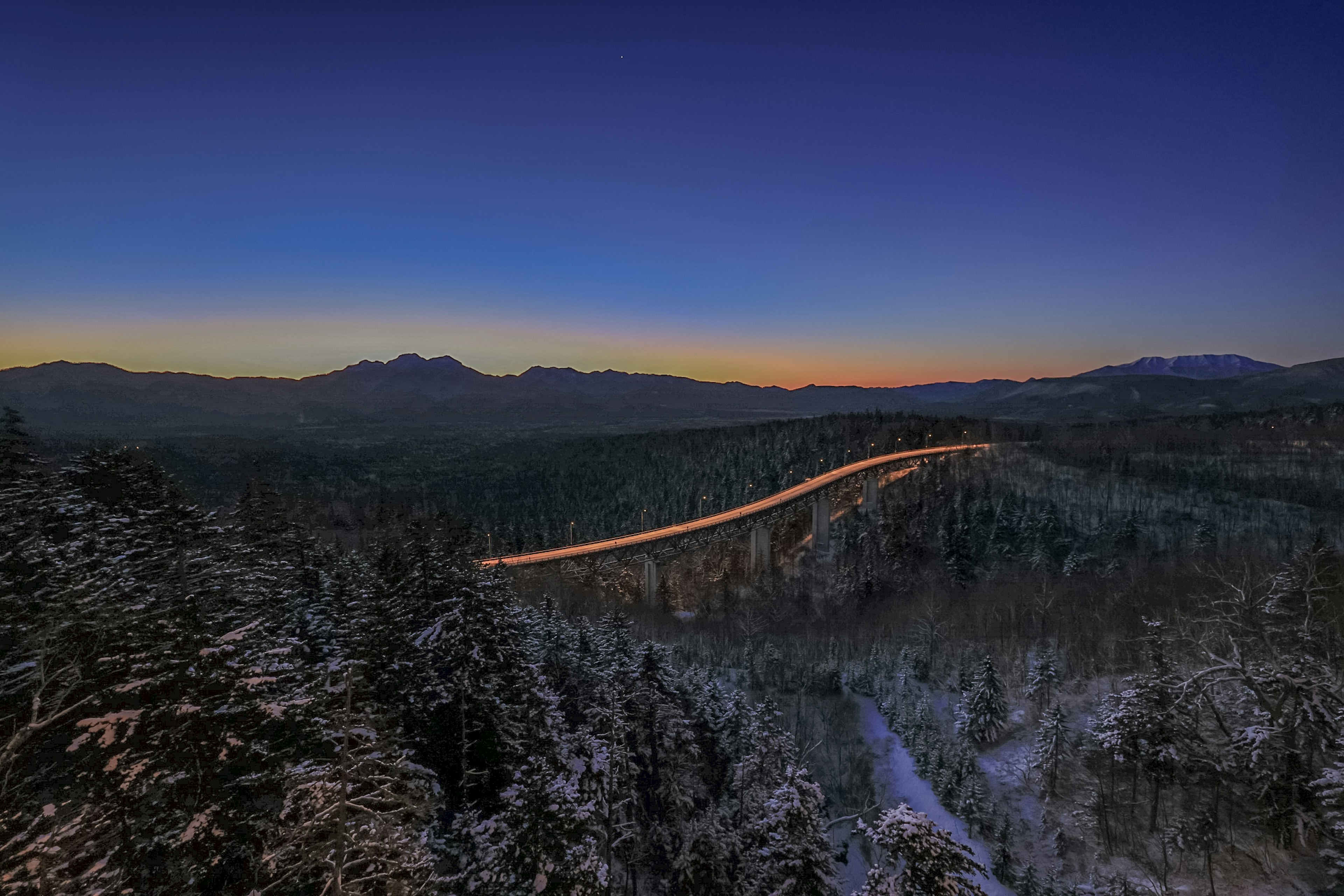 冬の山の風景と青い空に沿って曲がる道路