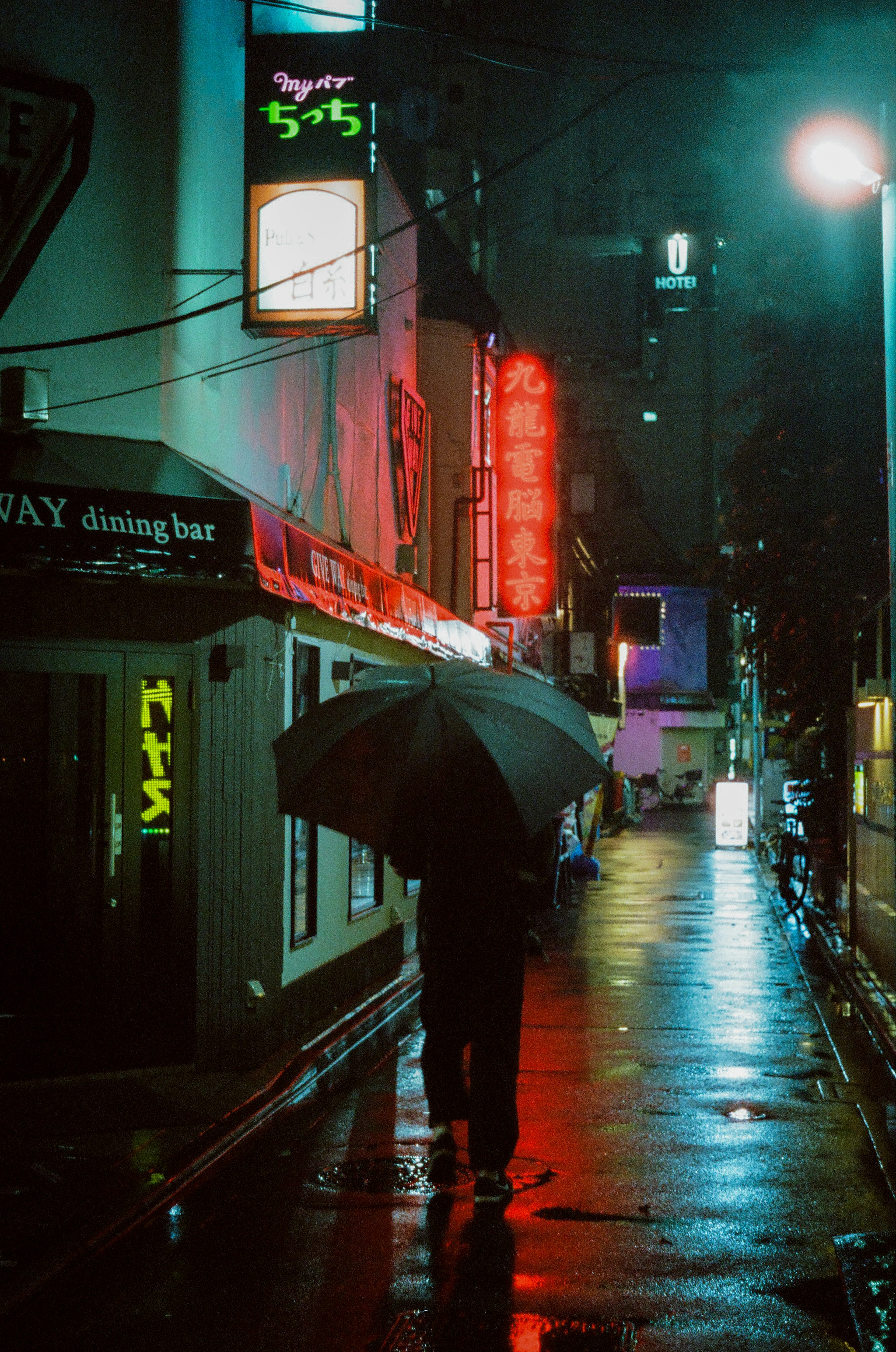 雨の中で傘をさした人が歩いている街の風景ネオンの看板が光る